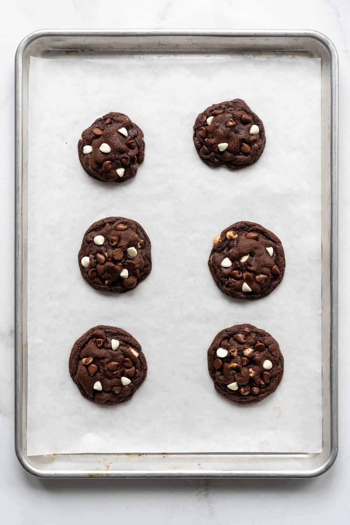 Six triple chocolate cookies on a baking sheet lined with parchment paper.