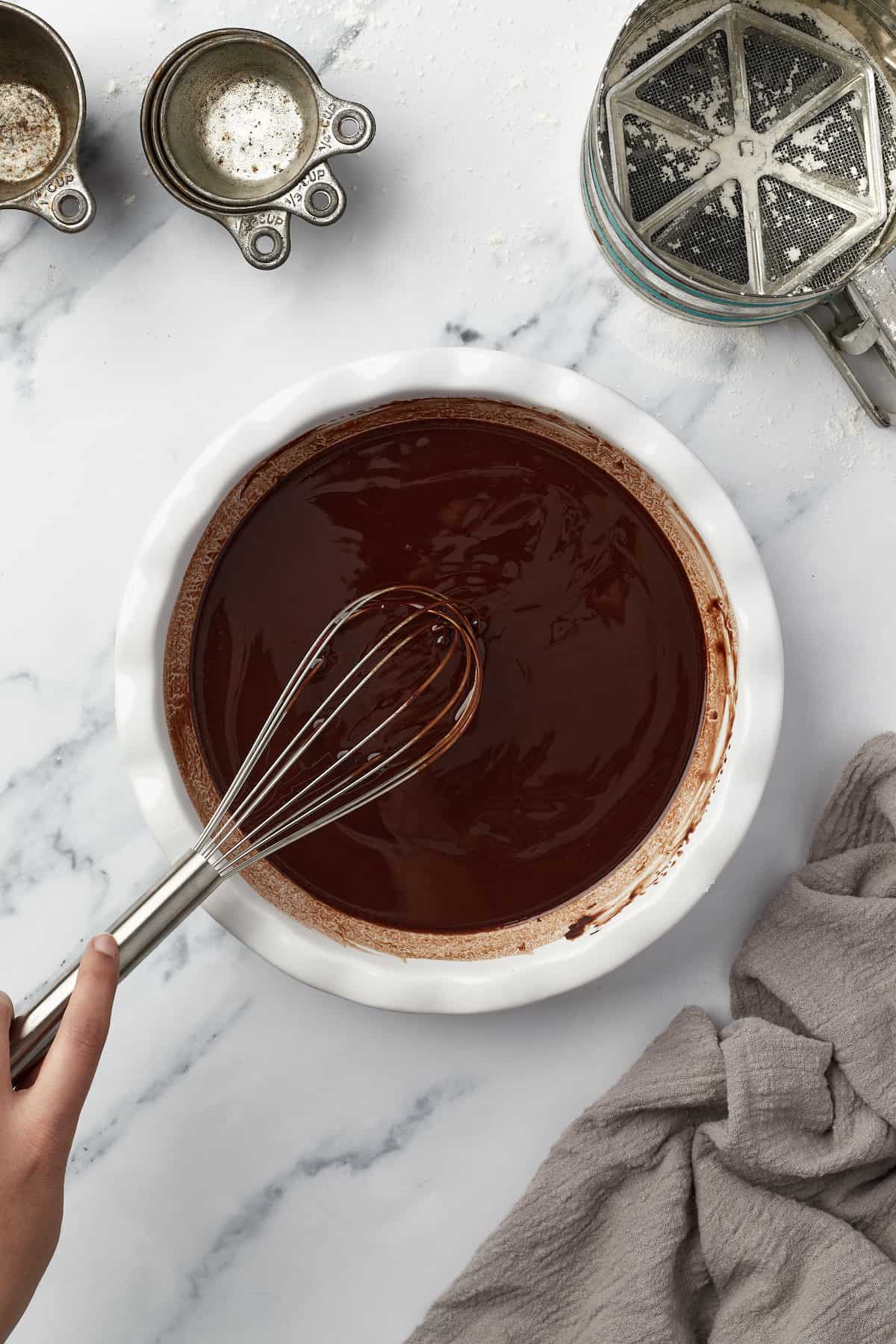 A bowl of melted chocolate and butter being stirred with a metal whisk