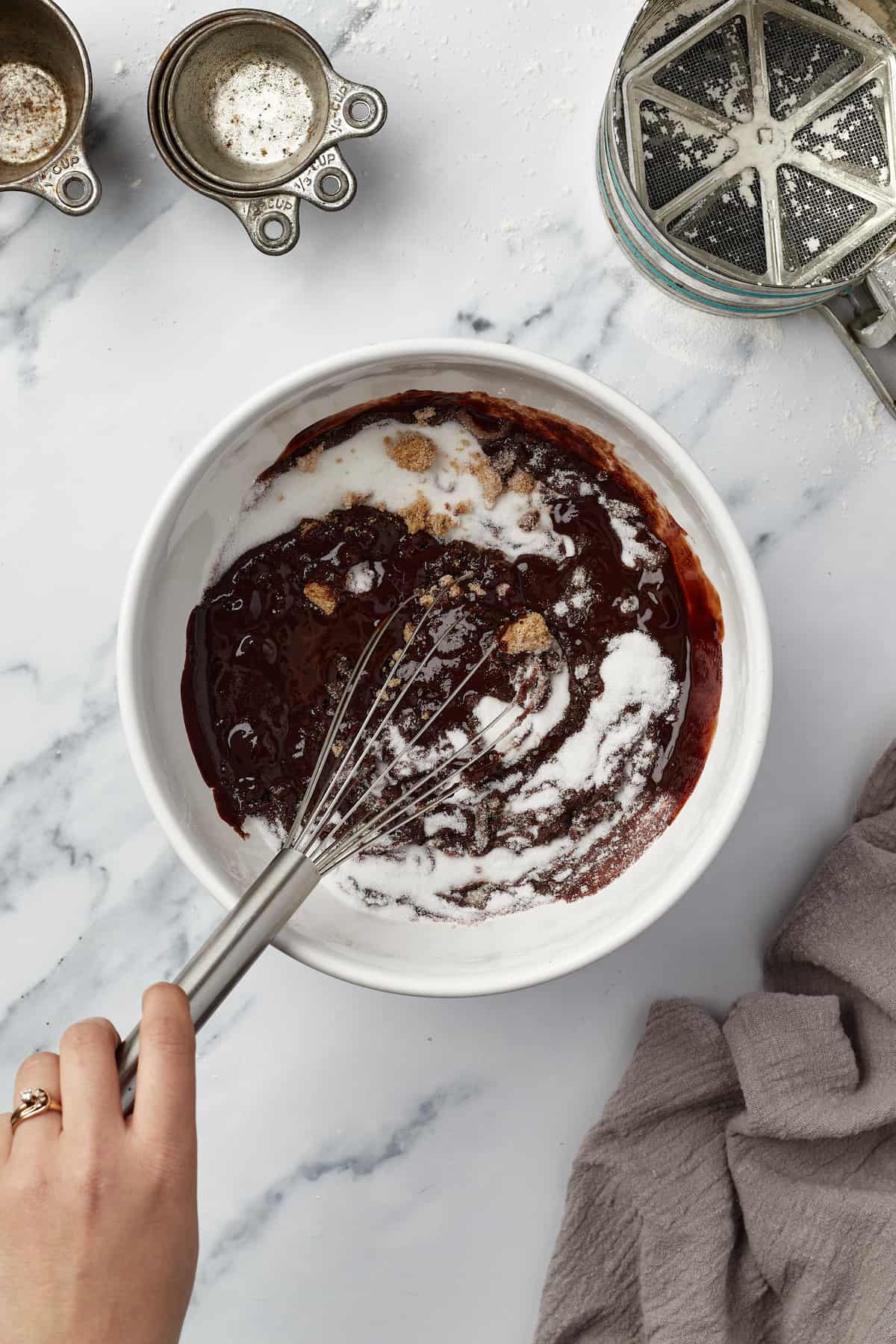A bowl of melted chocolate and butter being mixed with granulated sugar and light brown sugar
