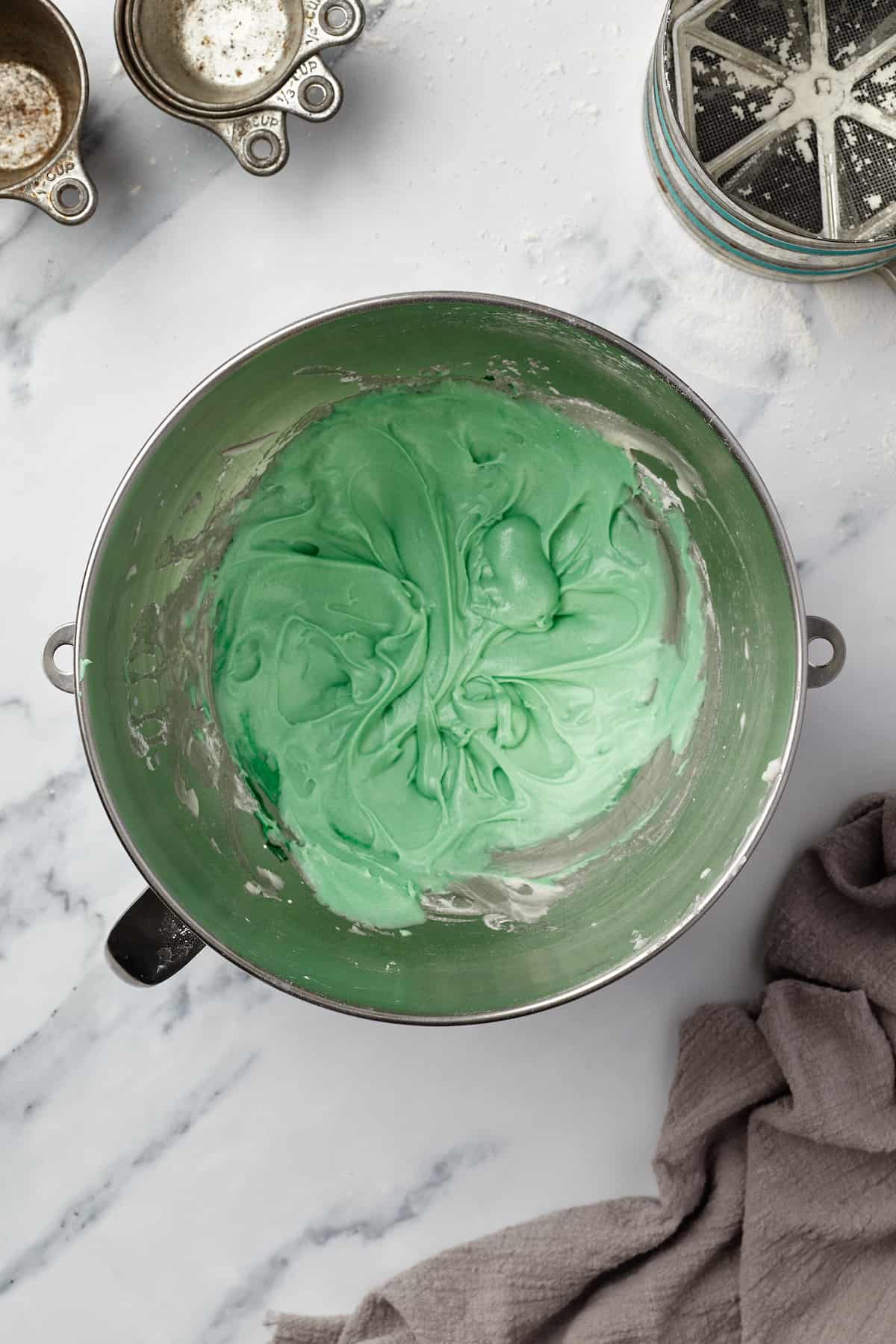 Mint frosting in a metal mixing bowl on a marble countertop