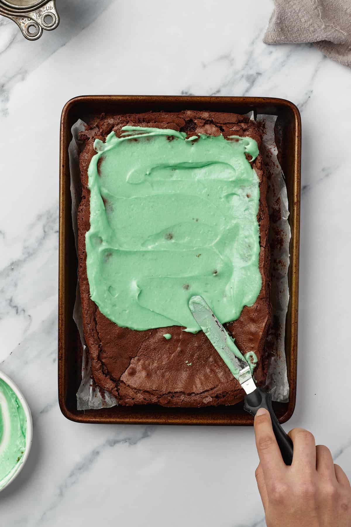 Mint frosting being spread onto a cooled batch of brownies