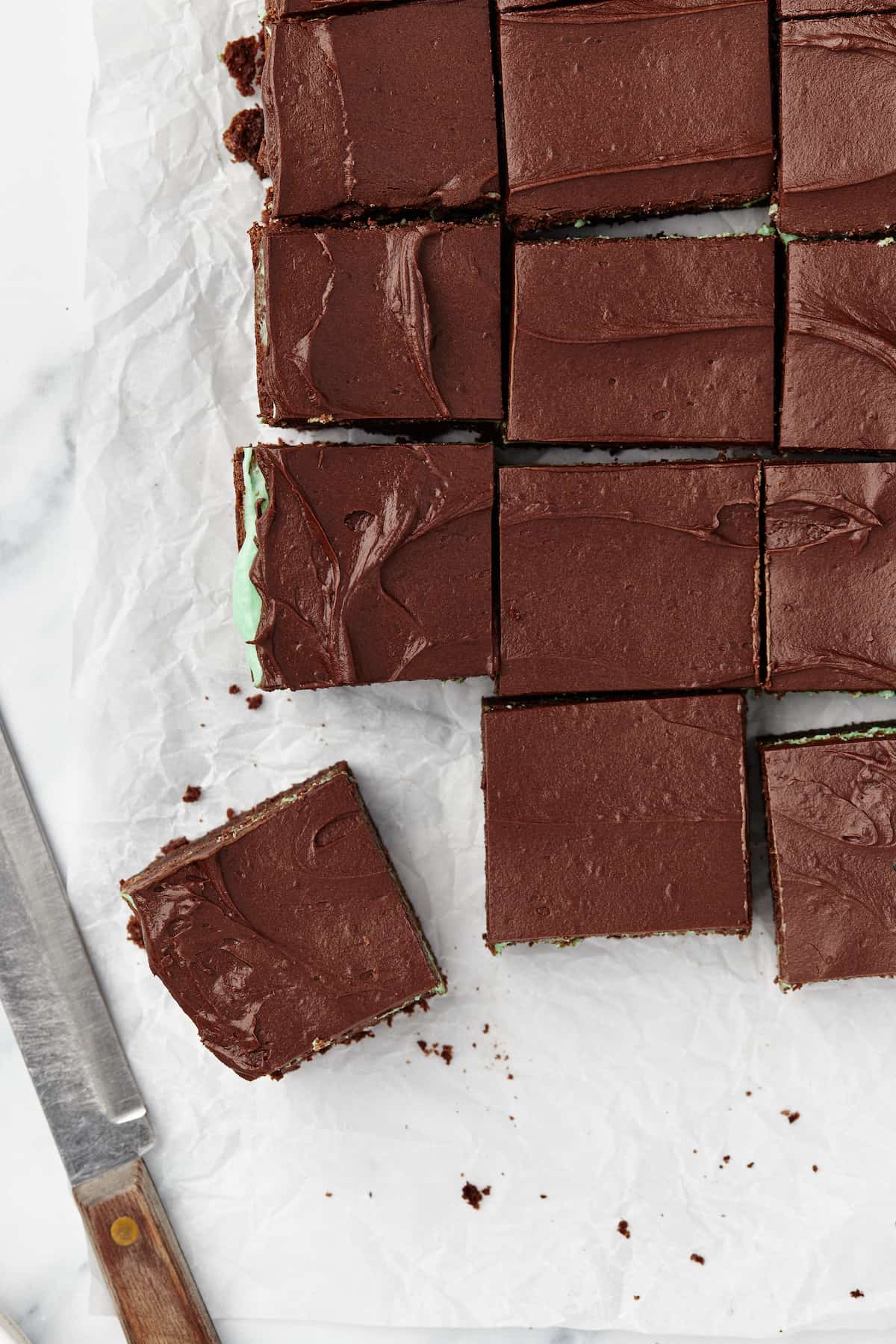 Twelve mint brownies on a piece of parchment paper next to a sharp kitchen knife
