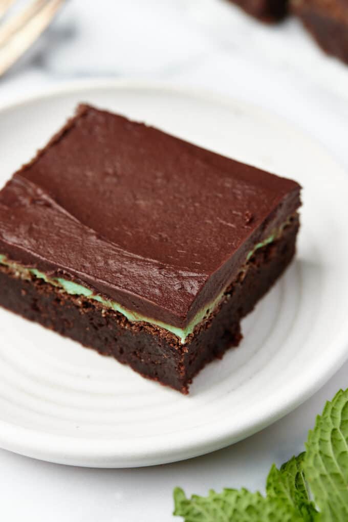 A close-up shot of a fudgy brownie with mint and chocolate frosting on top