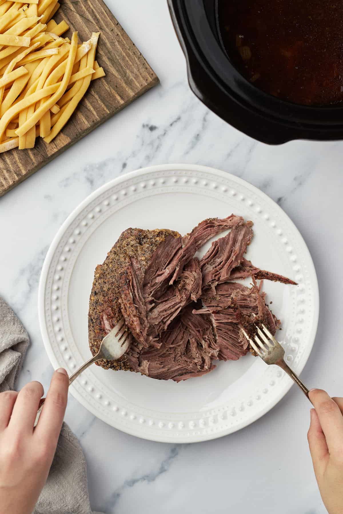 Two forks being used to shred up the slow-cooked chuck roast