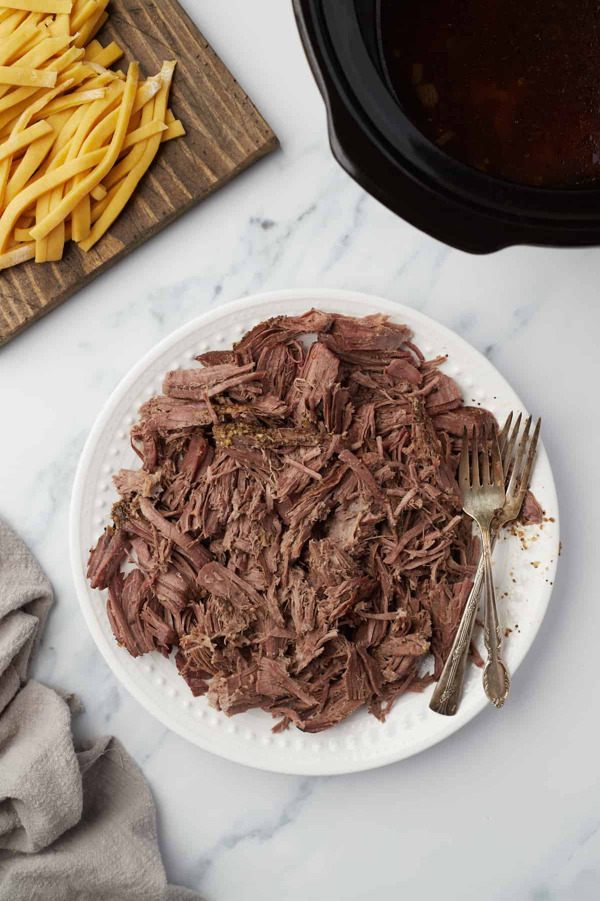 A plate full of shredded chuck roast with two forks beside the mound of meat