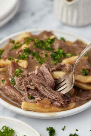 A close-up shot of a plate of slow cooker beef and noodles with a fork digging into some beef