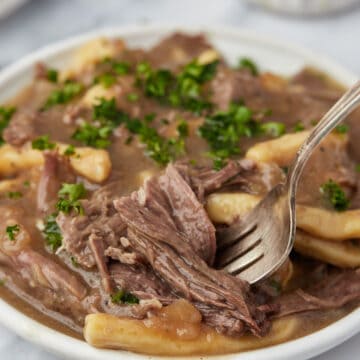 A close-up shot of a plate of slow cooker beef and noodles with a fork digging into some beef