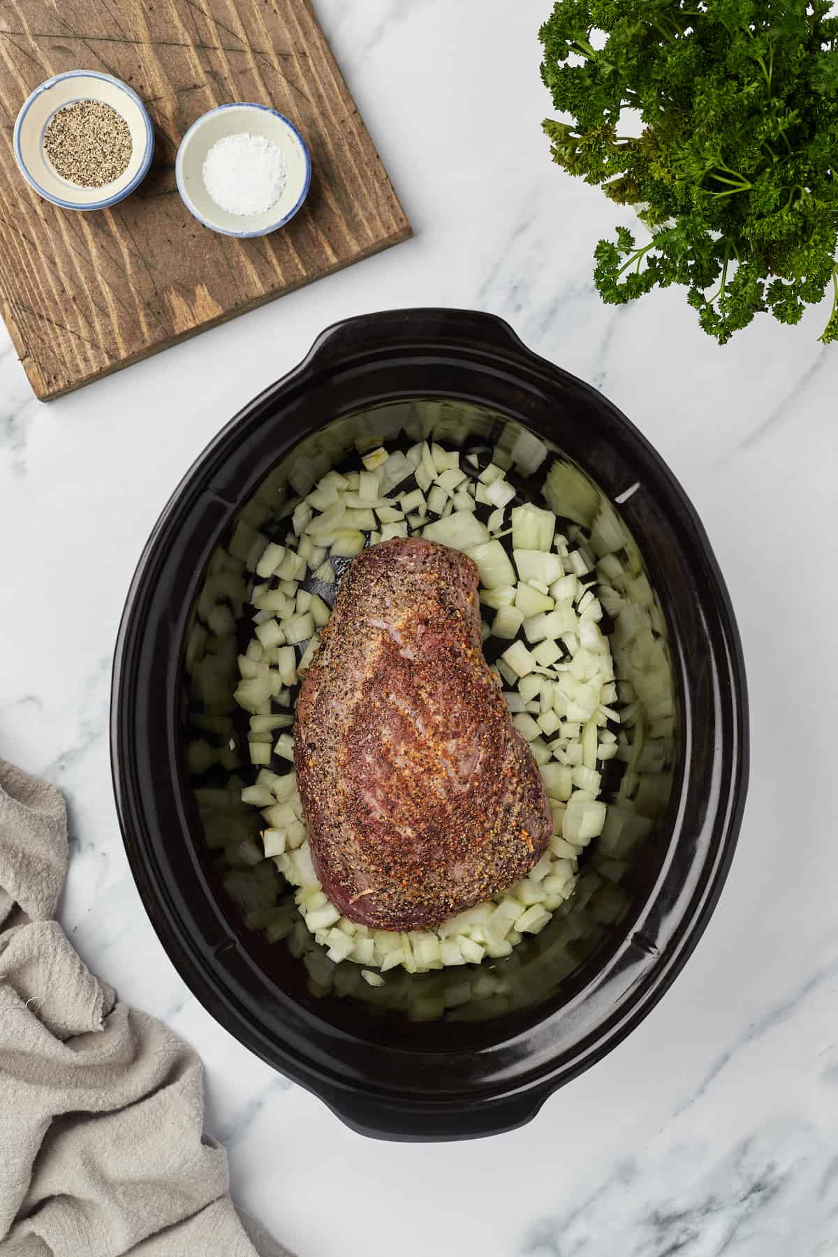 The browned chunk roast in a slow cooker with onions and garlic