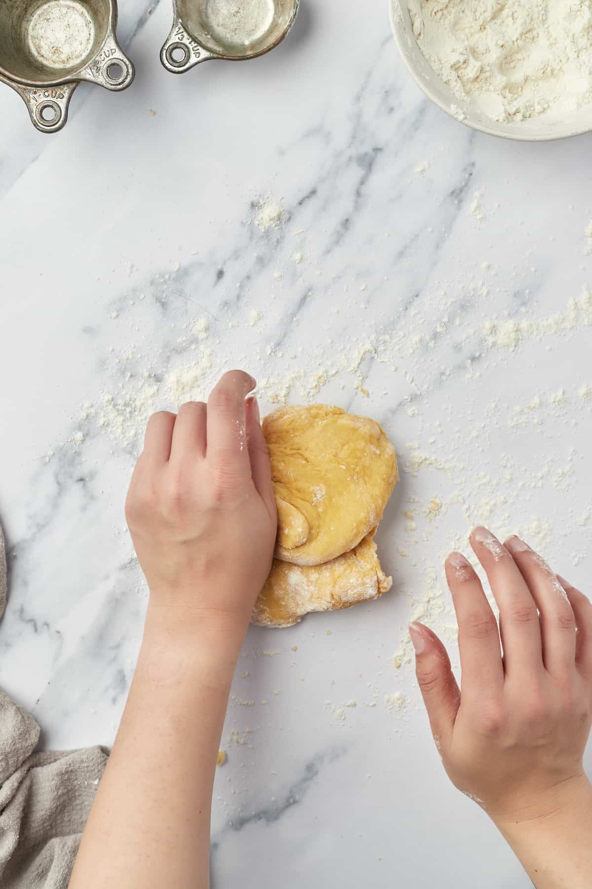 A hand kneading a batch of egg noodle dough on a marble countertop