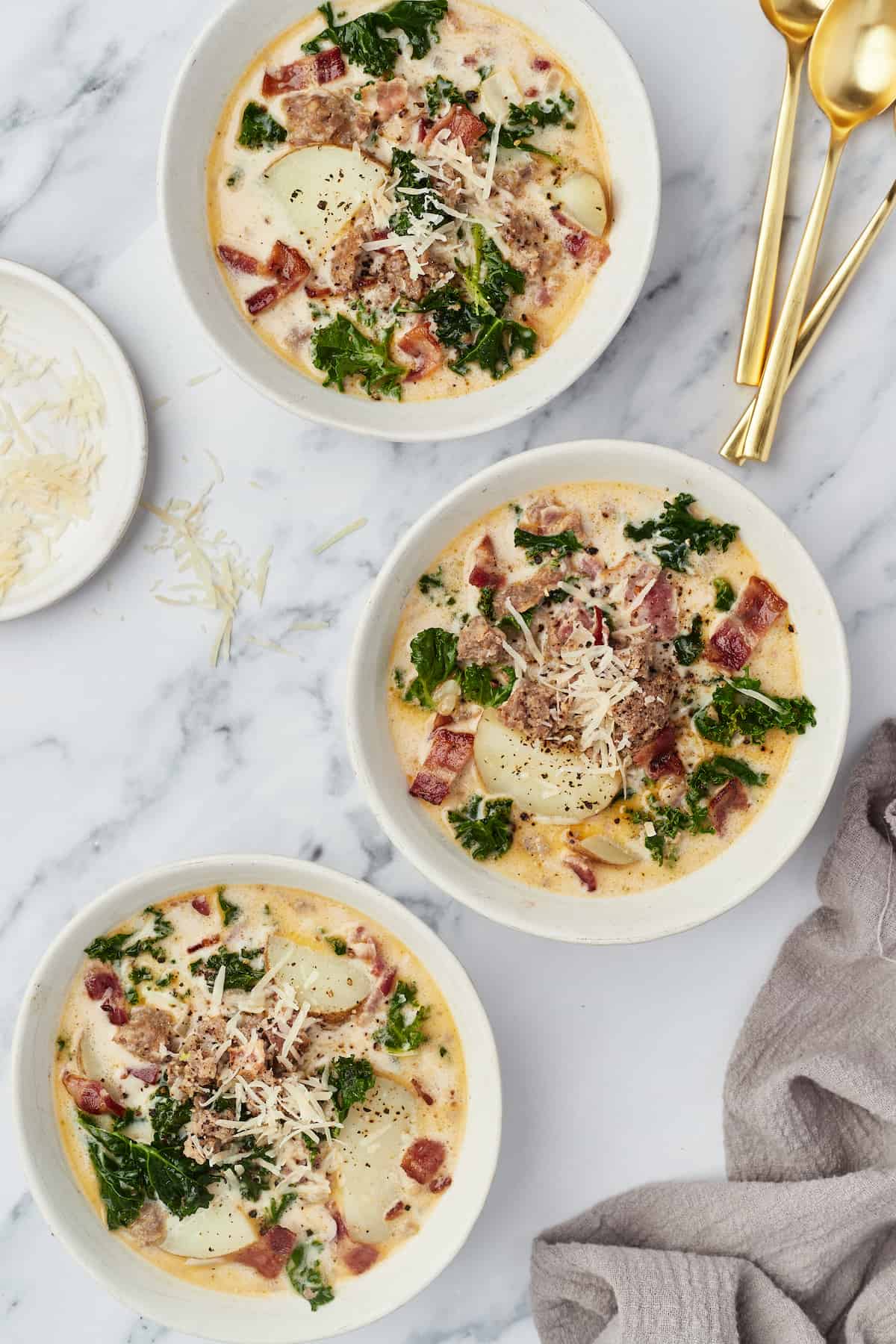 Three servings of Zuppa Toscana in three separate bowls on a marble countertop