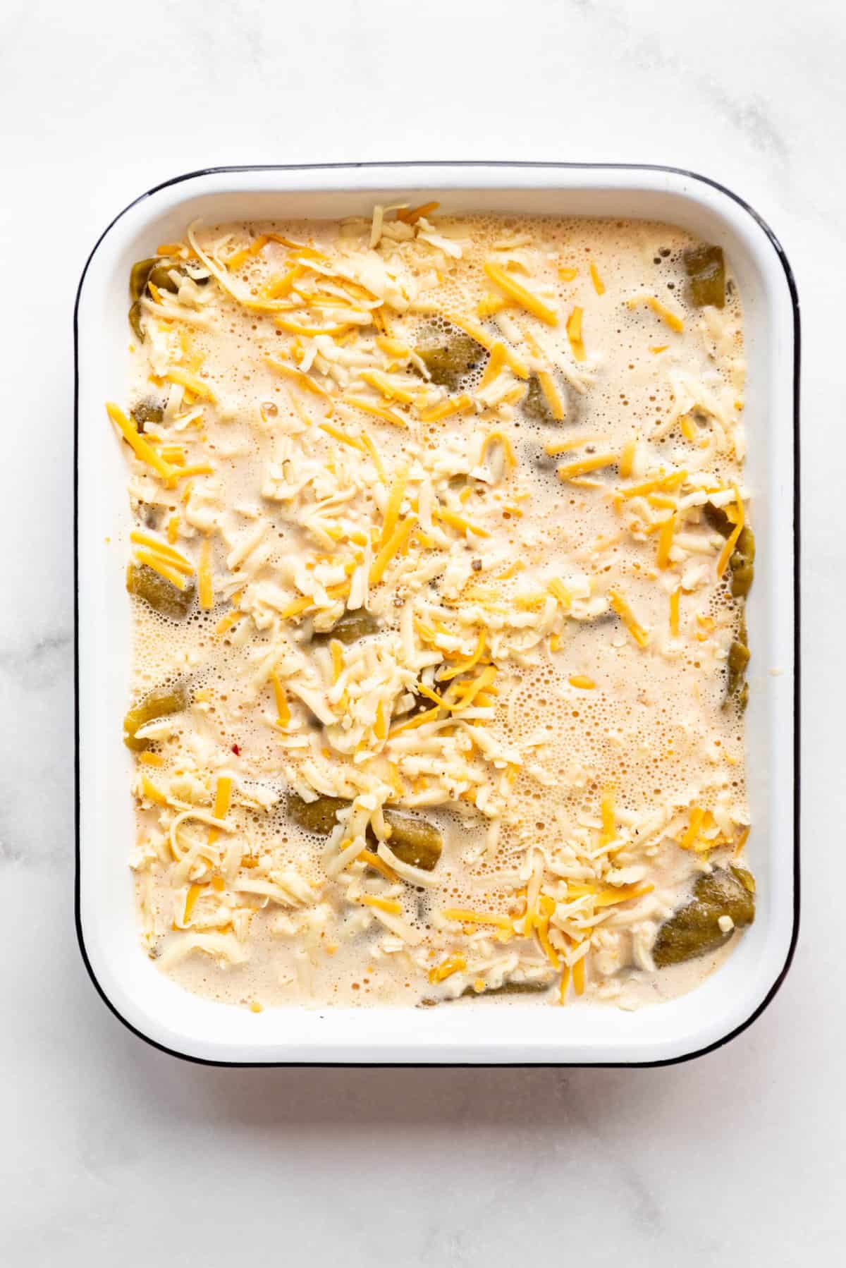 Pouring beaten eggs, milk, and spices over green chiles and cheese in a baking dish.