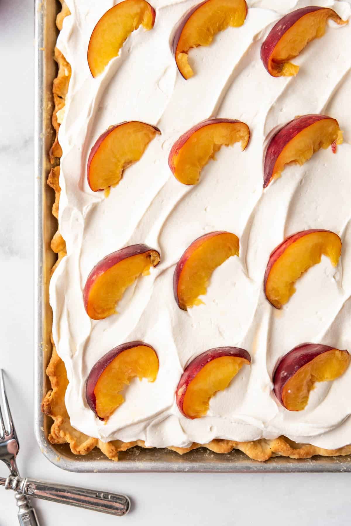 Fresh peach slices on top of whipped cream on a peach slab pie.