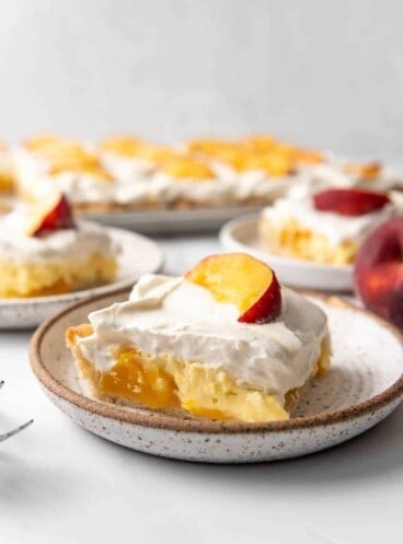 A slice of peaches and cream slab pie on an angle on a speckled plate.