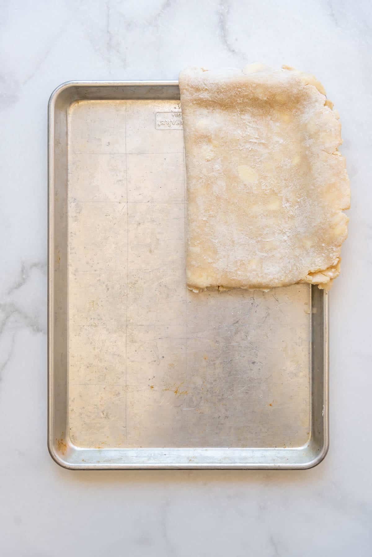 Laying a folded pie crust onto a large baking sheet.
