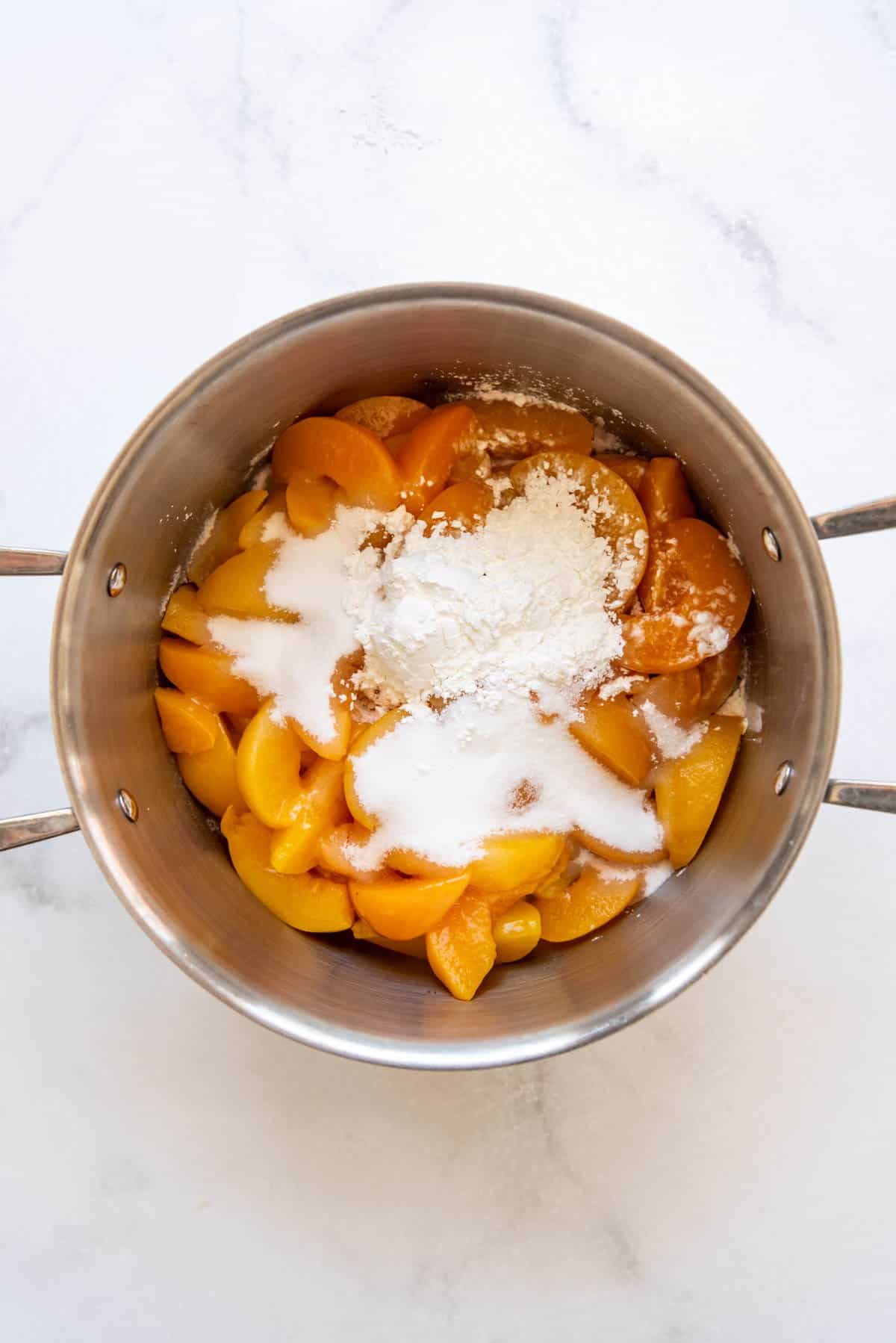 Adding sugar and cornstarch to peaches in a pot.