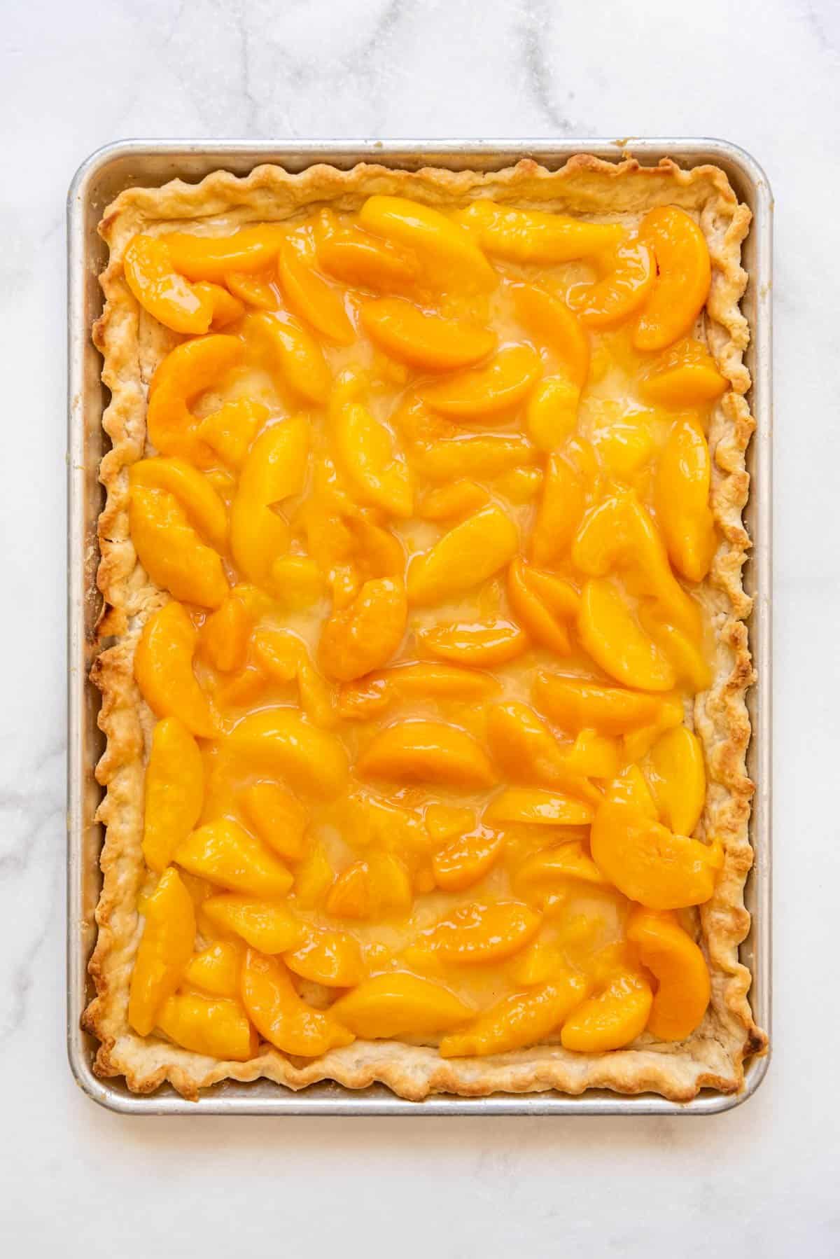 Peach pie filling spread on a baked pie crust in a baking sheet.