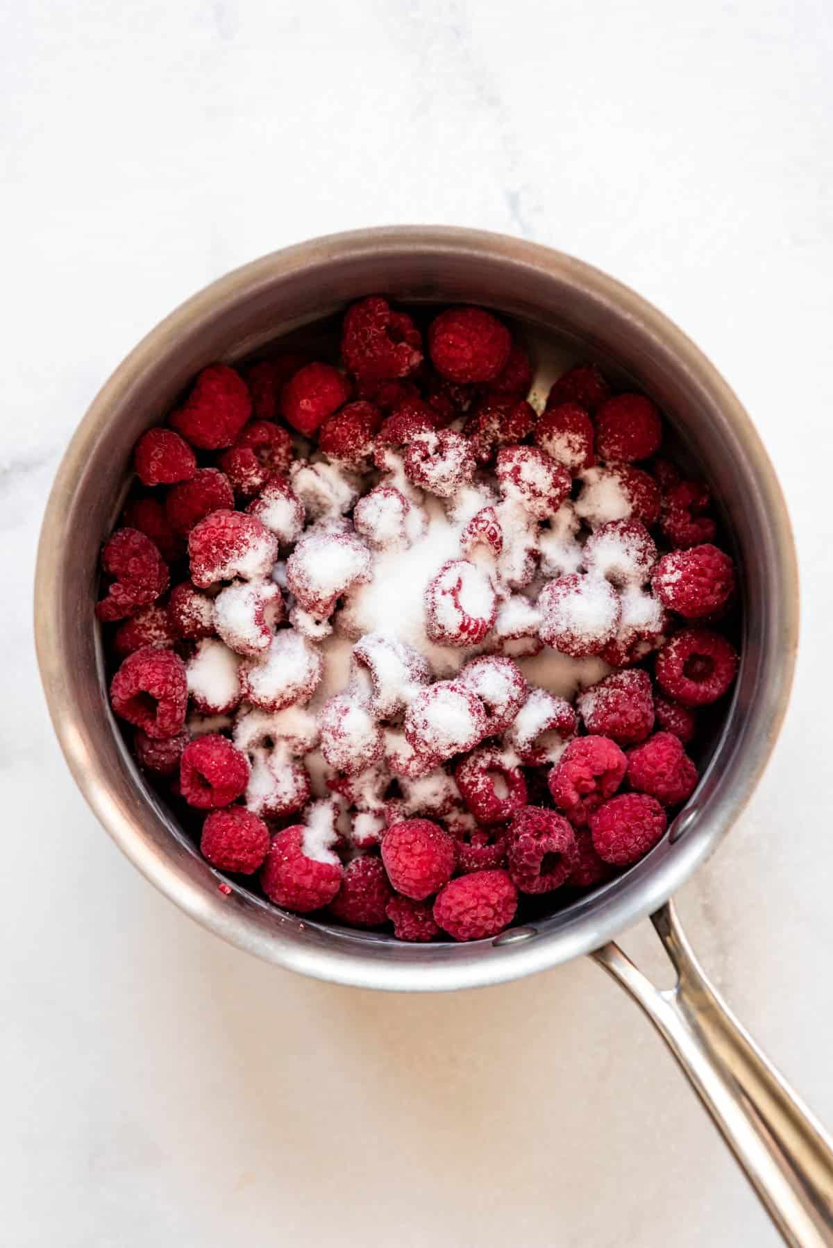 Adding sugar to frozen raspberries in a saucepan.