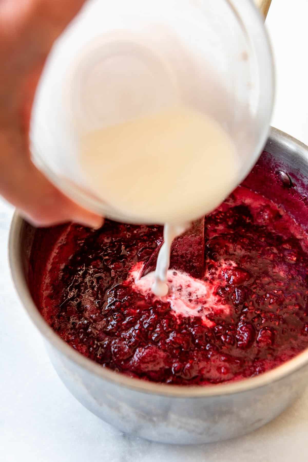 Adding a cornstarch slurry to cooked raspberries and sugar.