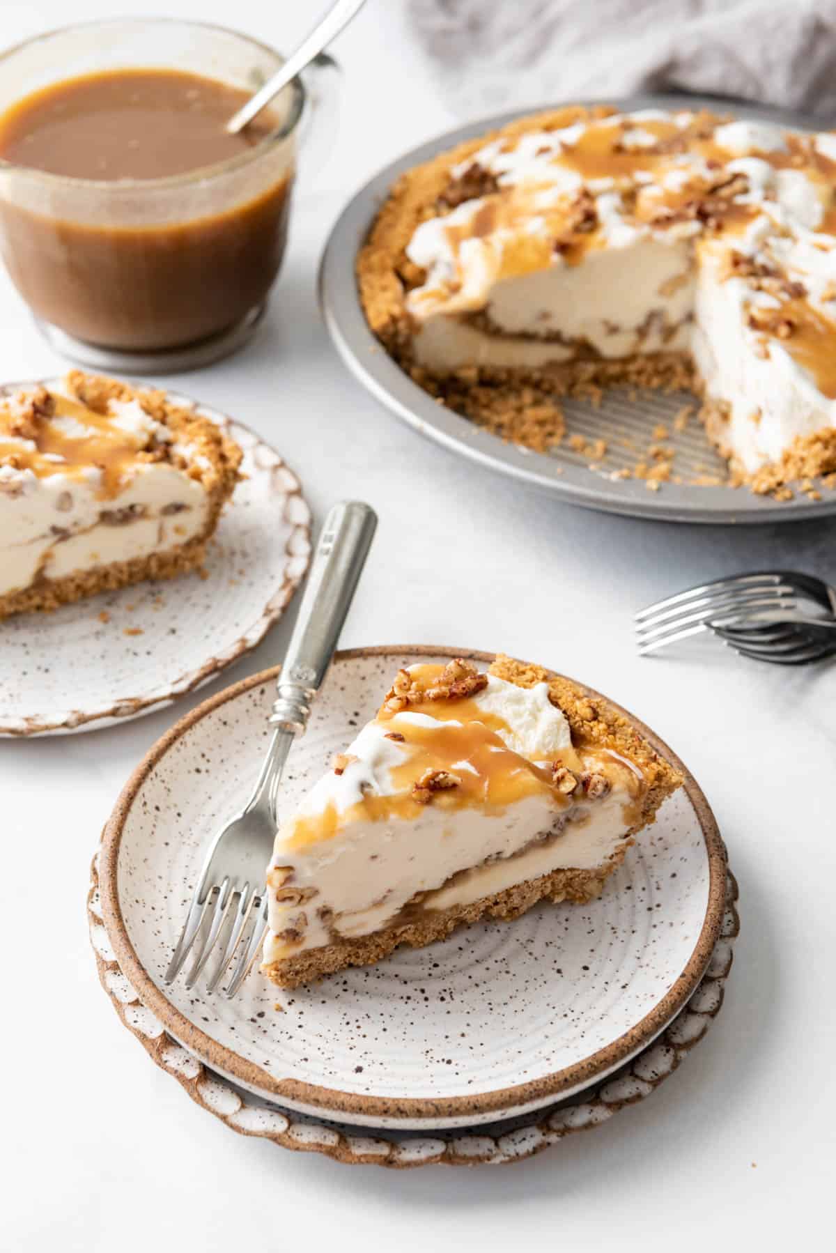 Slices of butter pecan ice cream pie on plates in front of the rest of the pie.