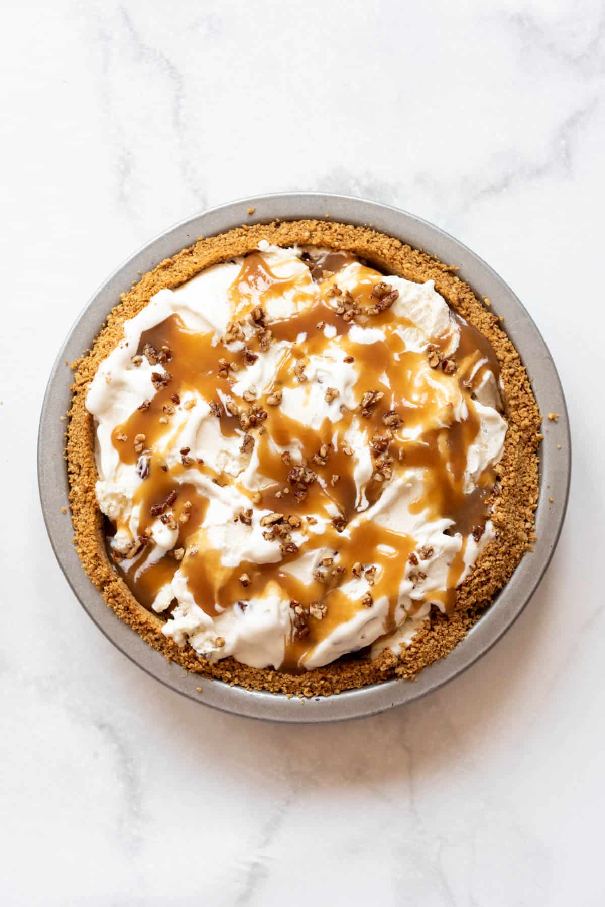 Butterscotch sauce and chopped pecans sprinkled over a frozen ice cream pie.