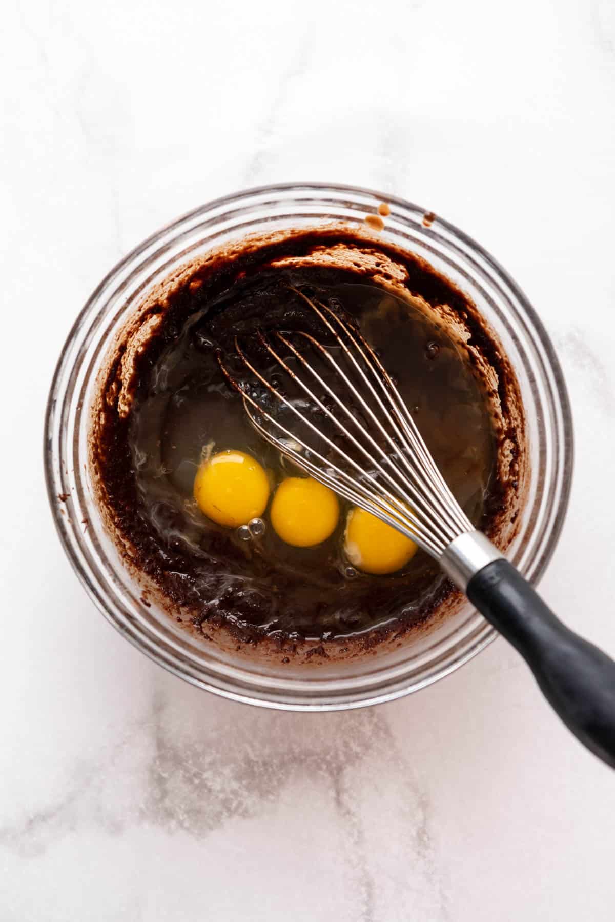 3 eggs in a bowl of brownie batter with a whisk.