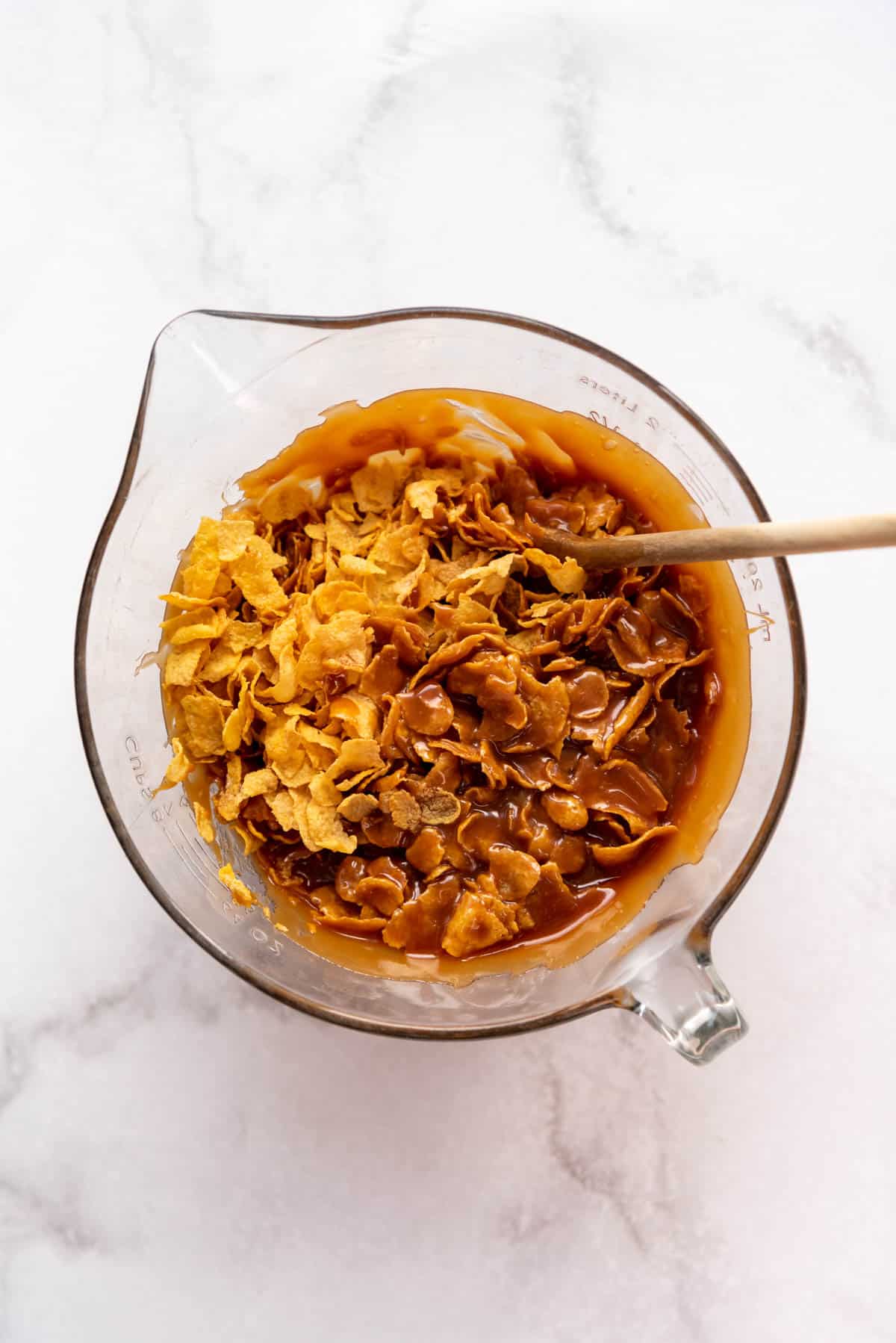 Stirring cornflakes and homemade caramel together in a large white bowl.