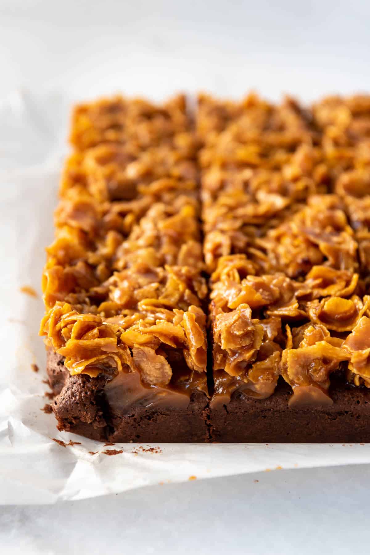 Homemade fudge brownies topped with a caramel cornflake mixture on parchment paper.