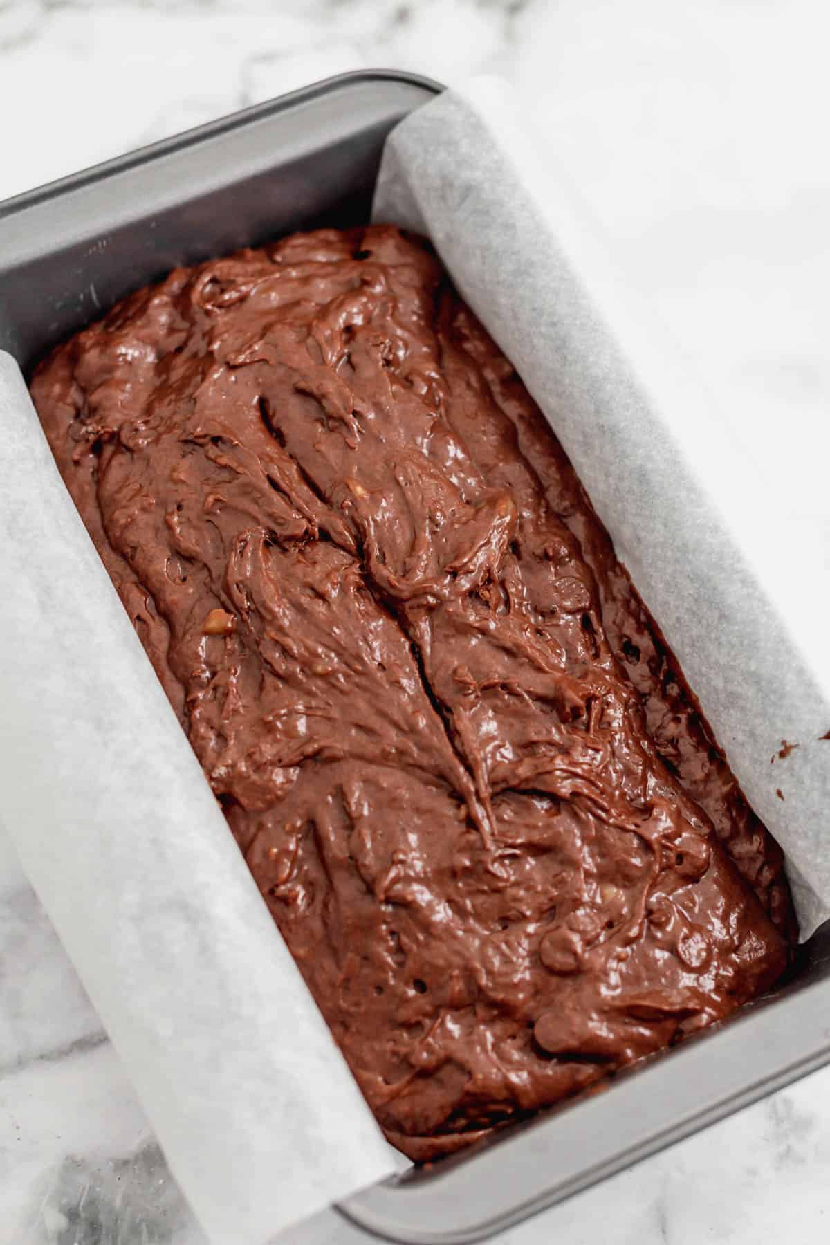 Chocolate banana bread batter in a bread pan lined with parchment paper.