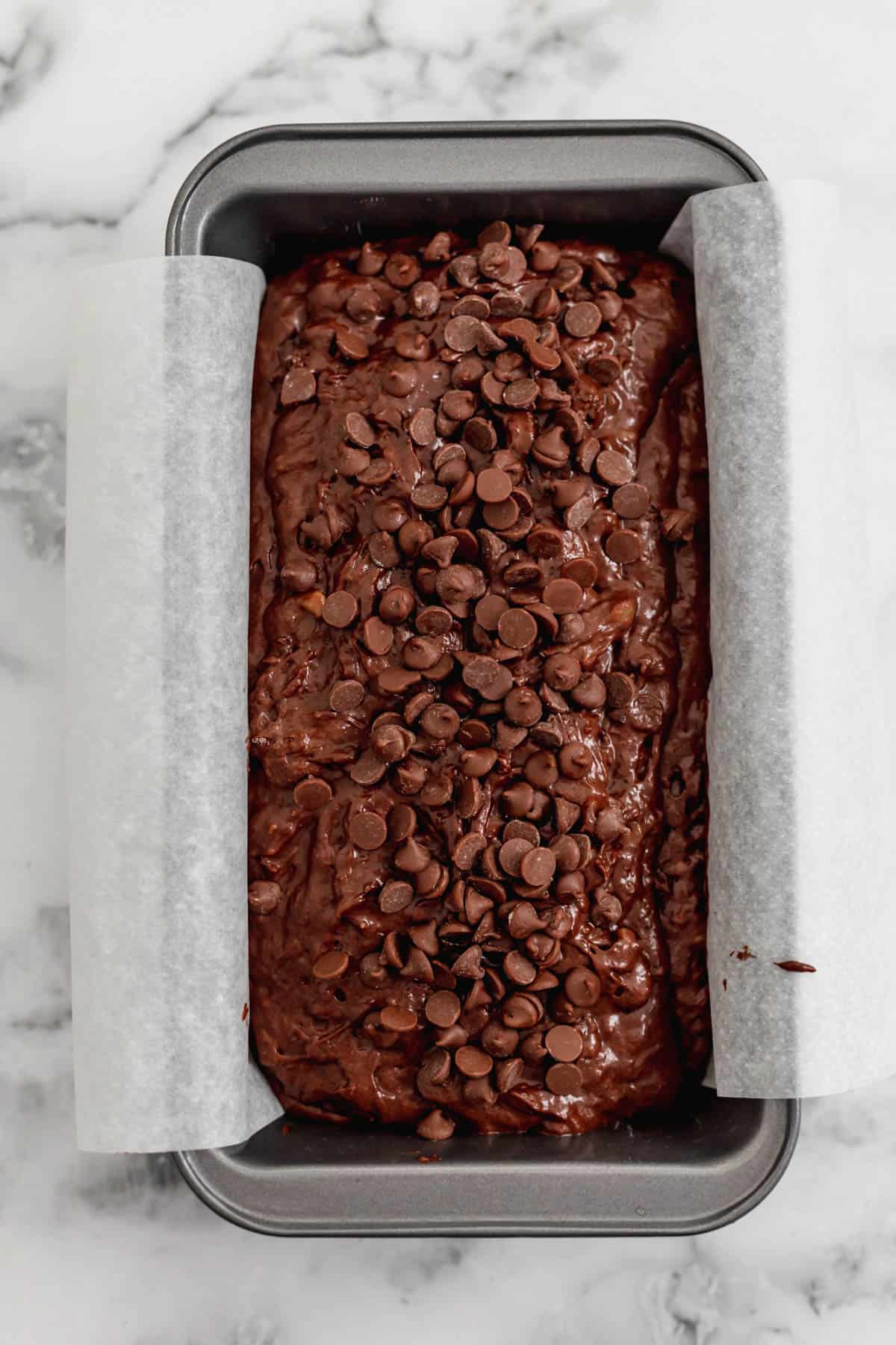 Chocolate banana bread in a bread pan with chocolate chips on top.