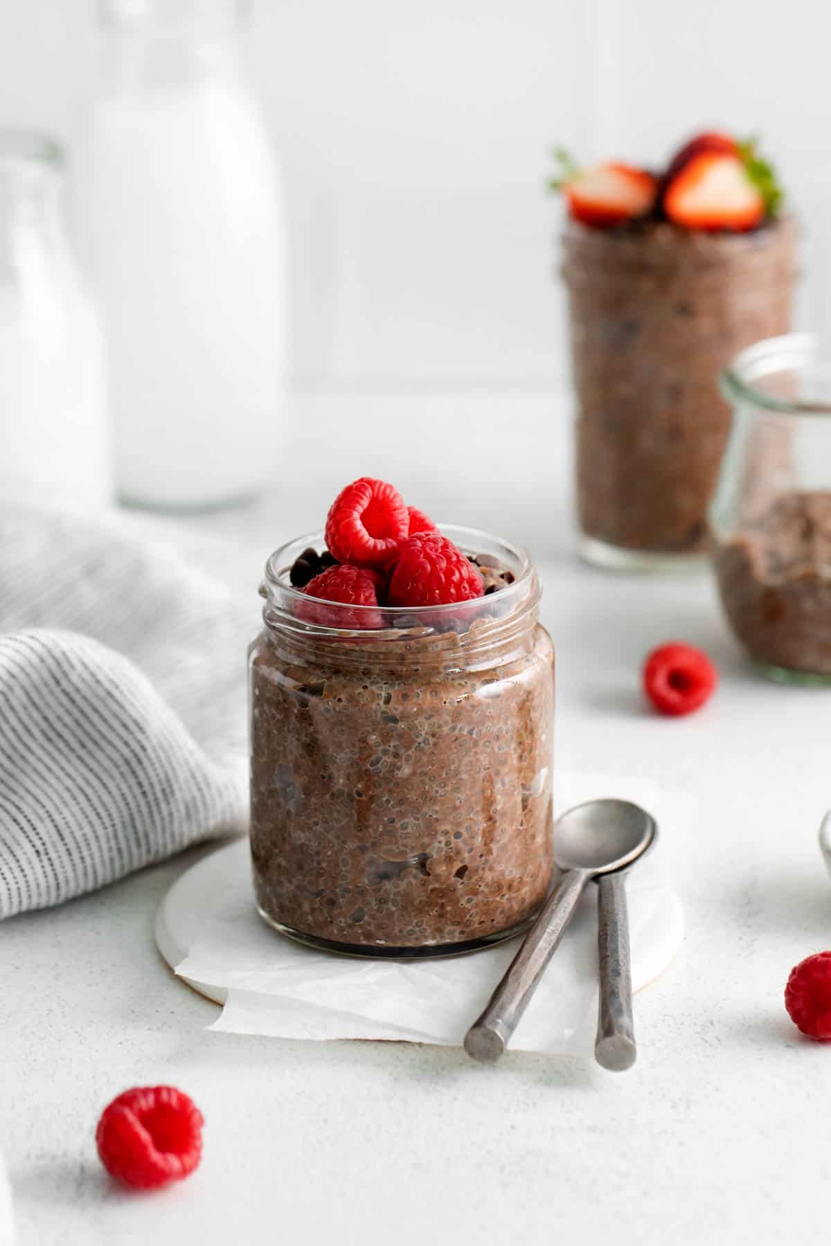 Raspberries on top of chocolate chia pudding with spoons next to it and more chia seed pudding behind it.
