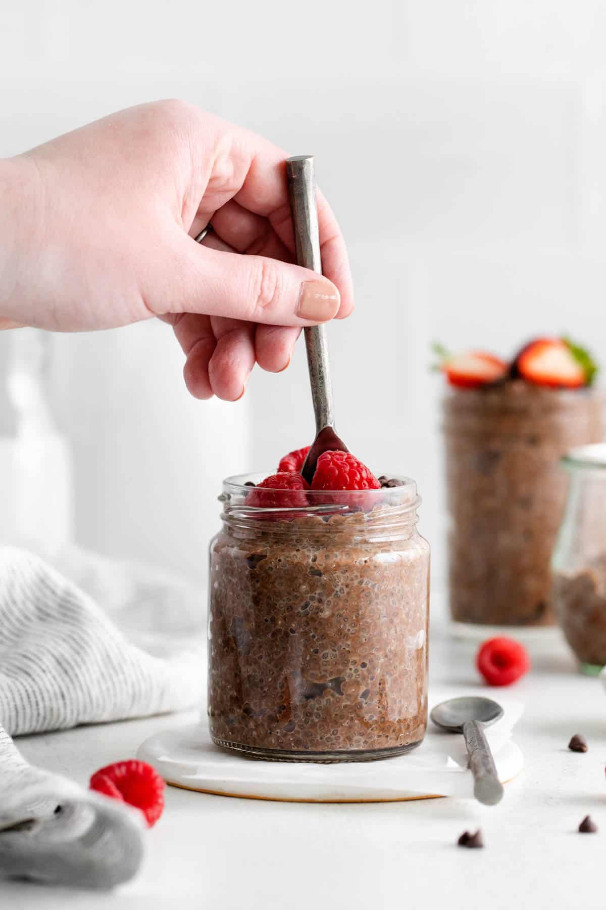 A hand holding a spoon scooping chocolate chia pudding from a jar.
