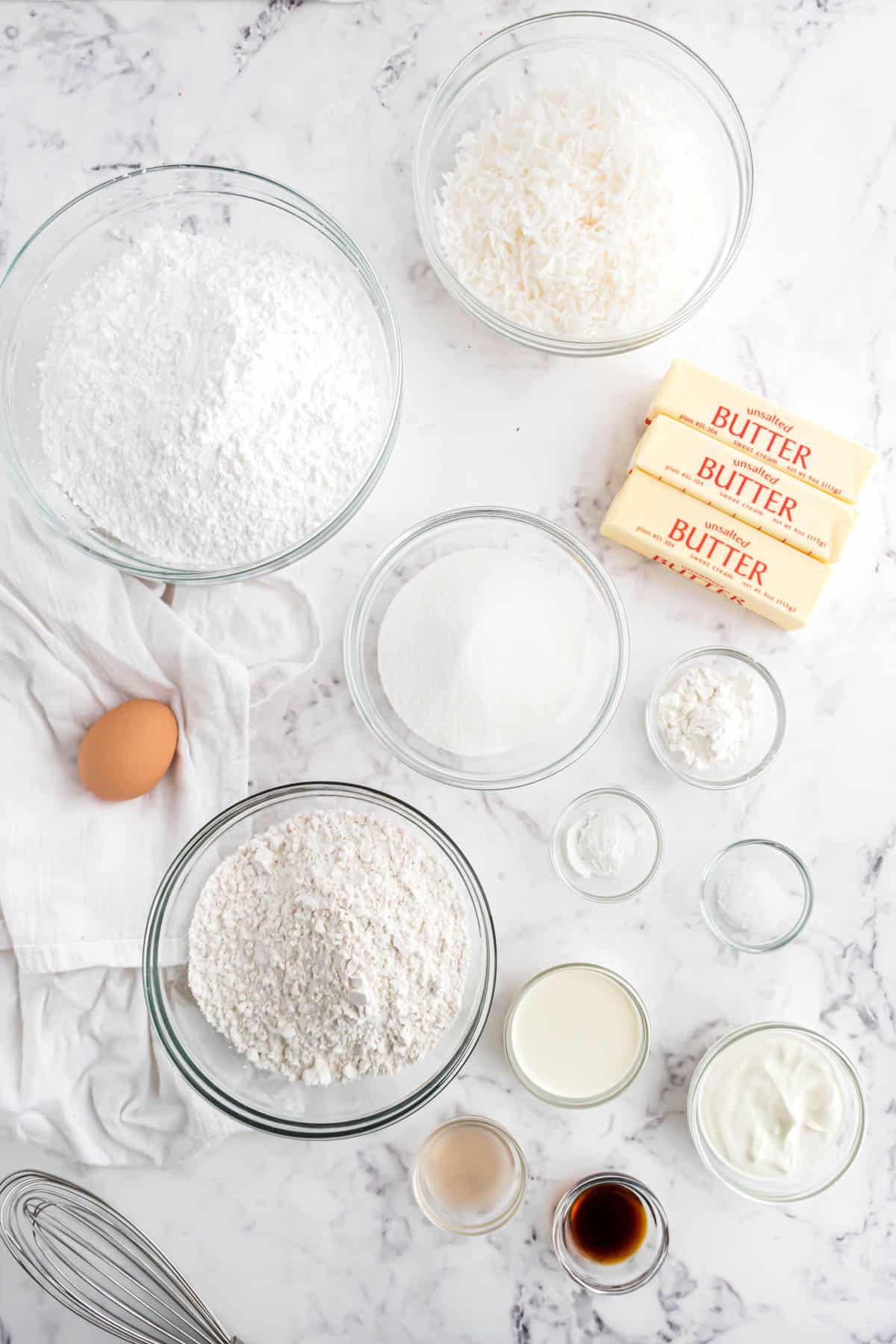 Ingredients for frosted coconut sugar cookie bars in separate bowls on a white marble surface.