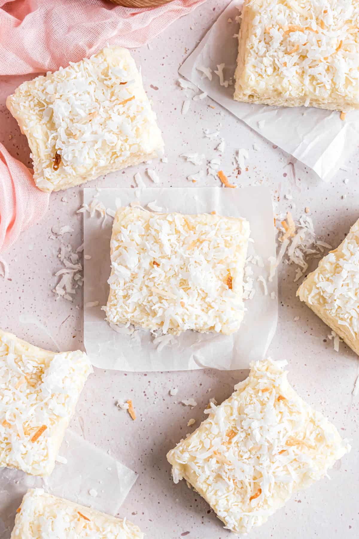 Frosted coconut sugar cookie bars with sweetened shredded coconut sprinkled on top and around them.