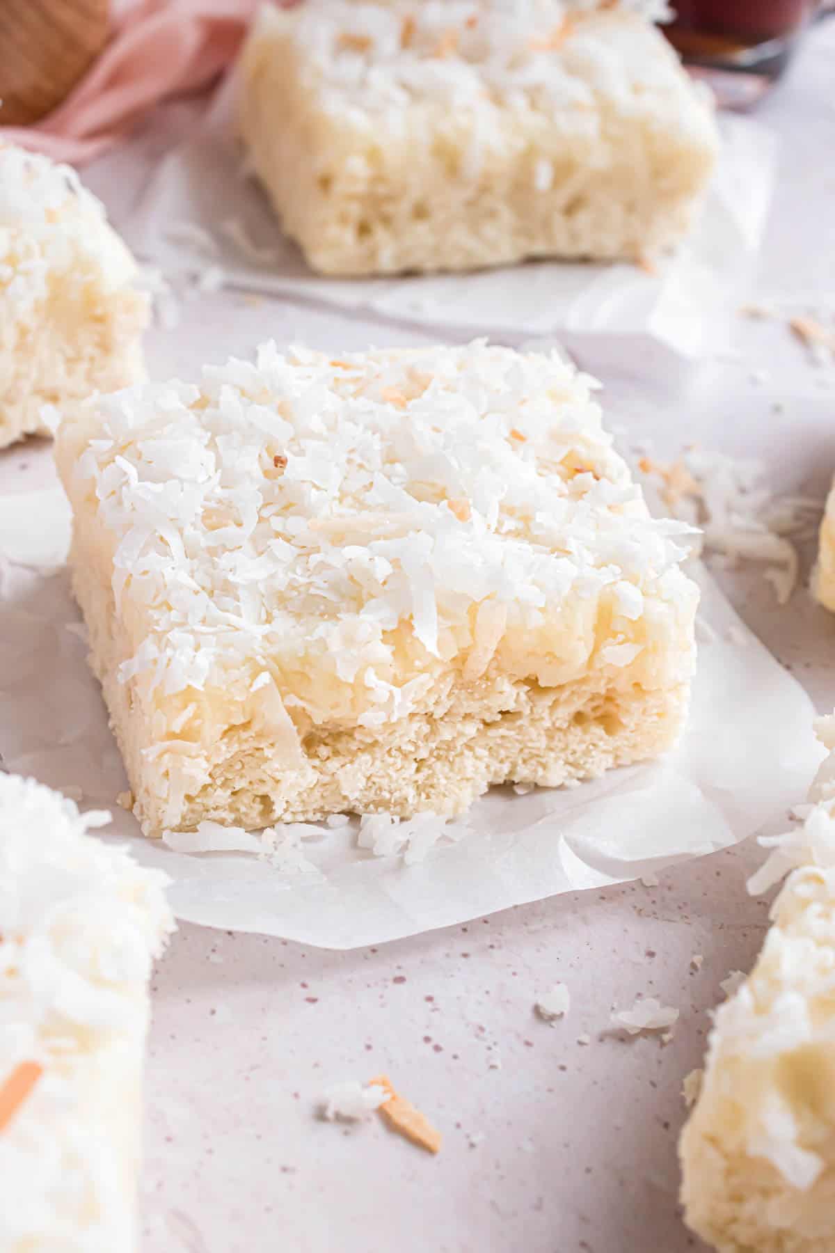 A frosted coconut sugar cookie bar on a square of parchment paper.