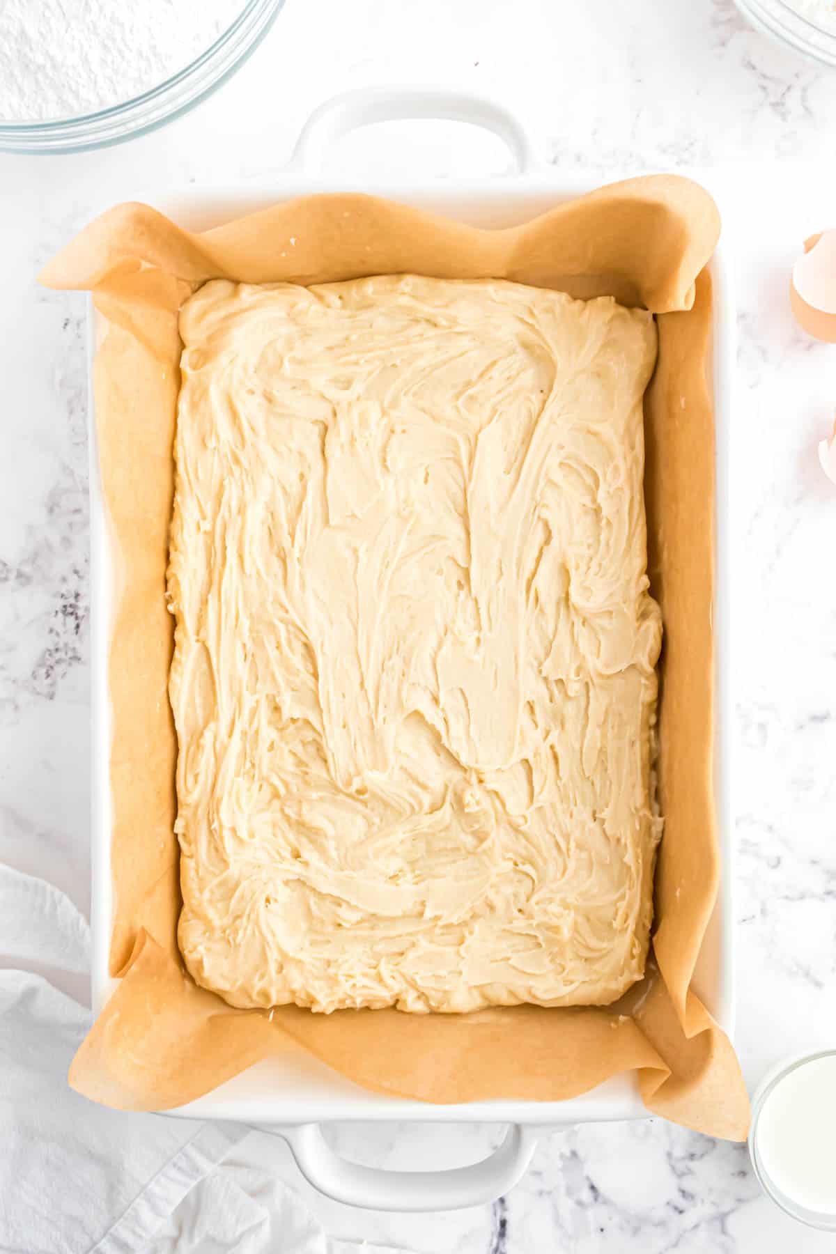 Sugar cookie dough spread into a white baking dish lined with a parchment paper sling.