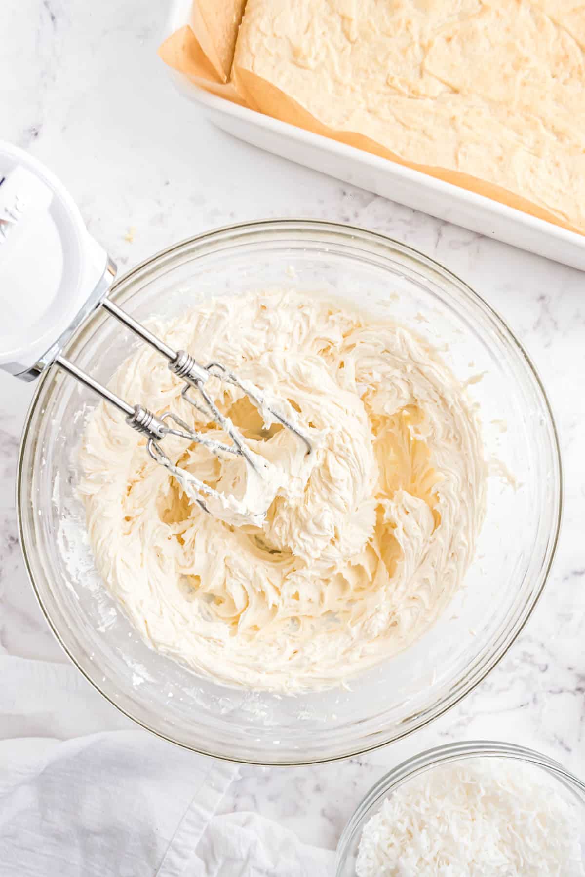 A hand mixer beating frosting in a glass bowl.