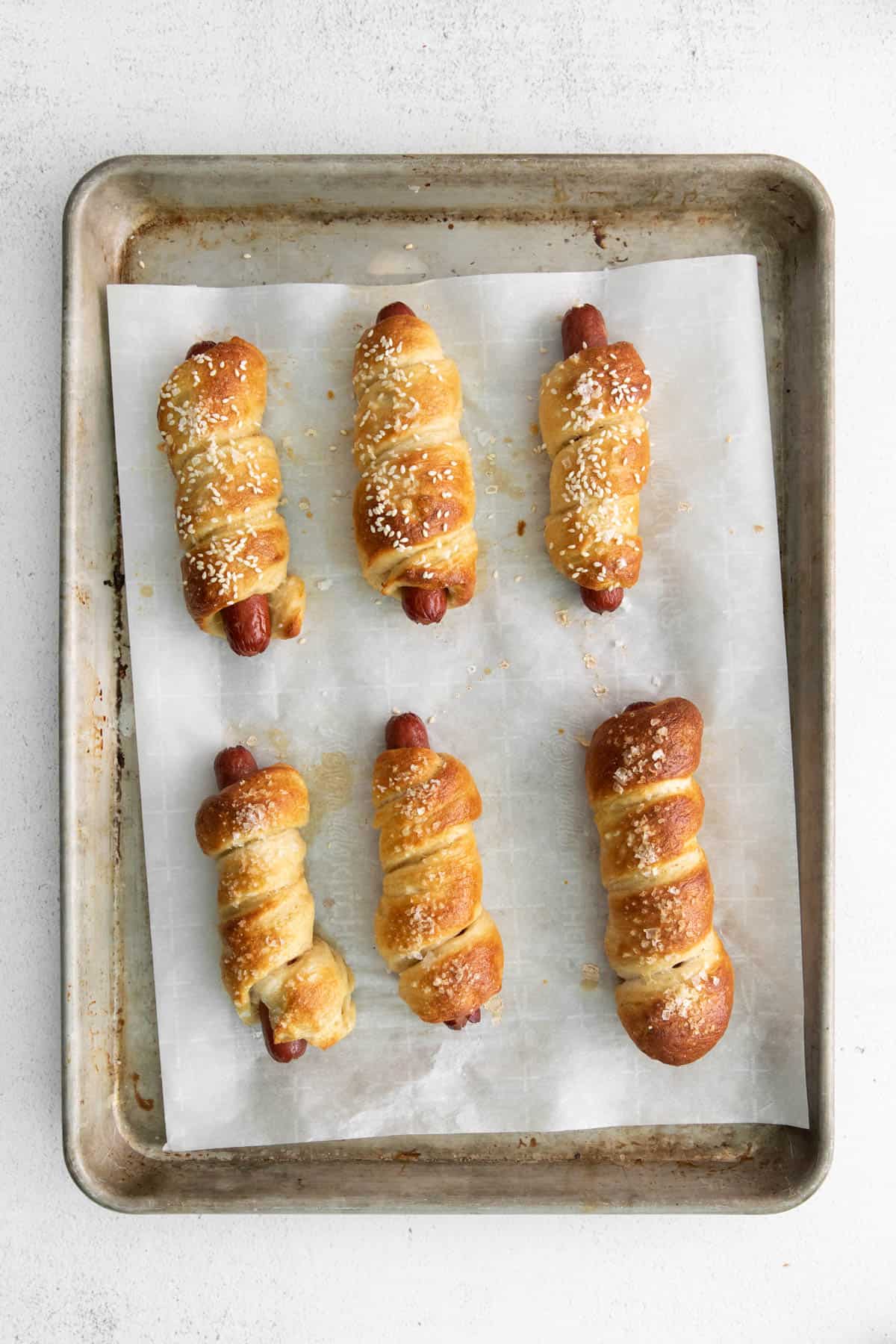 Baked pretzel dogs topped with salt on a baking sheet.