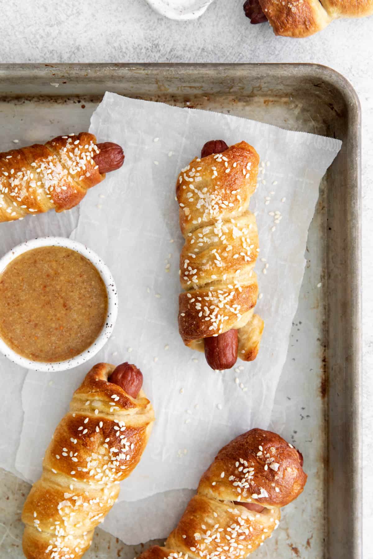 Pretzel dogs on a baking sheet with parchment paper next to a bowl of spicy honey mustard dipping sauce.
