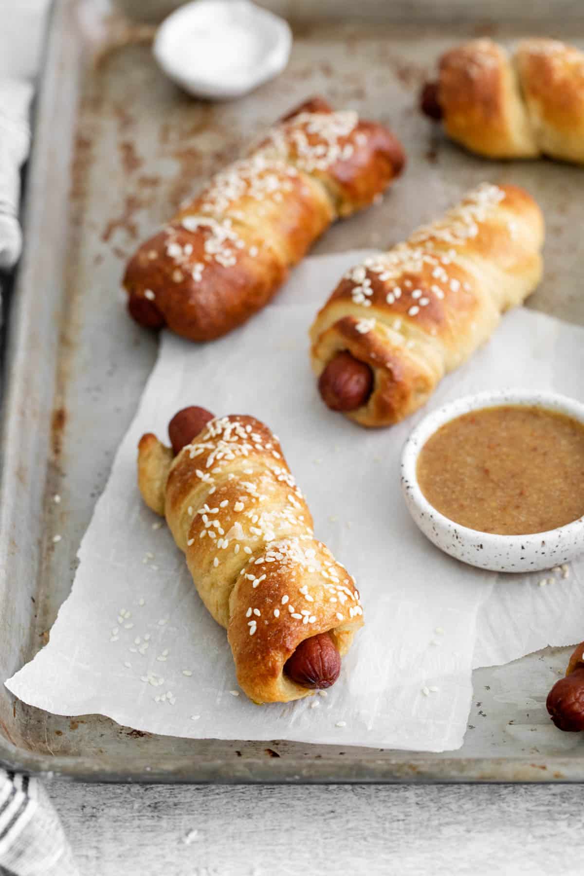 Homemade soft pretzel dogs on a baking sheet.