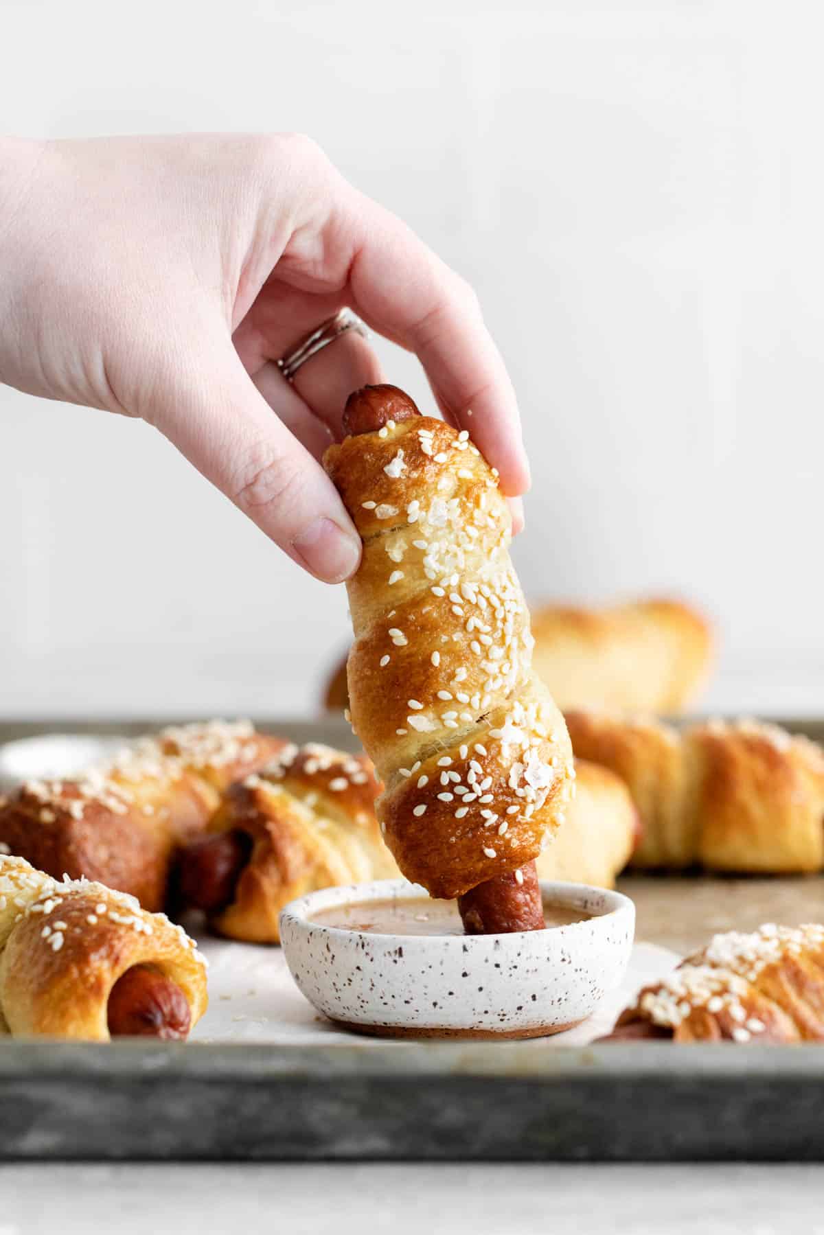 A hand holding a pretzel dog dipping it into a spicy honey mustard sauce.