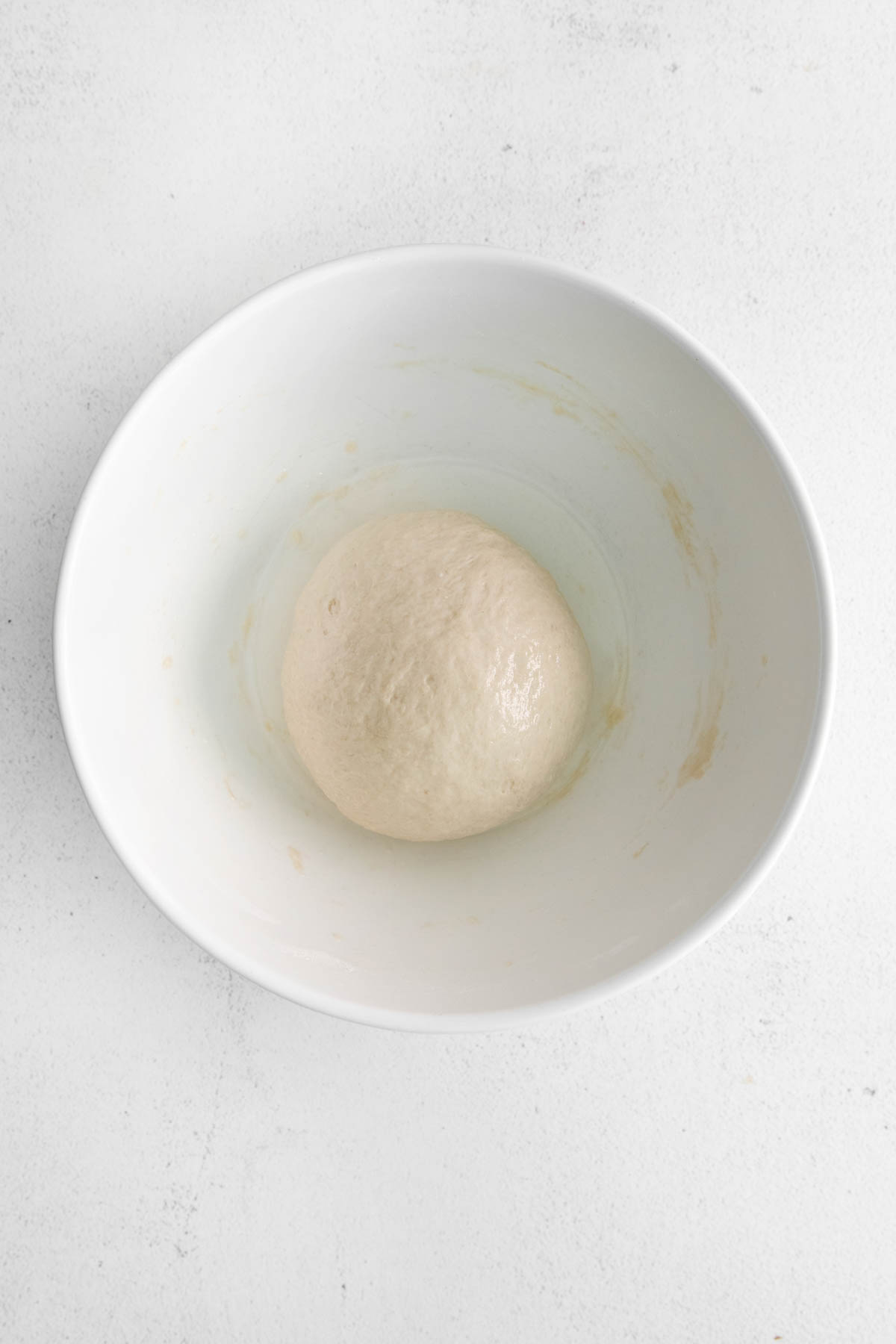 A ball of soft pretzel dough in a white bowl before rising and doubling in volume.