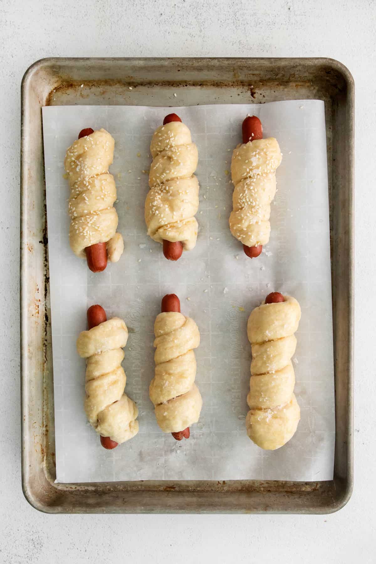 Hot dogs wrapped in pretzel dough on a baking sheet.