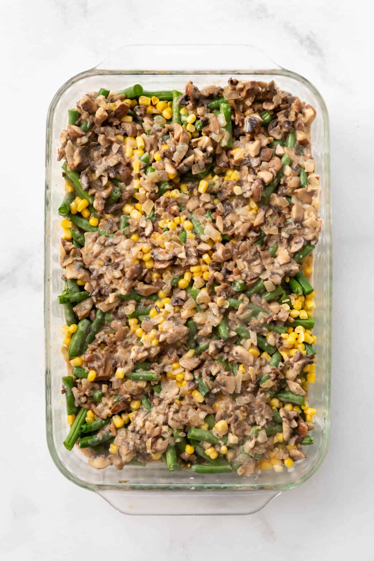 Ground beef in a creamy sauce spread over green beans and corn in a casserole dish.
