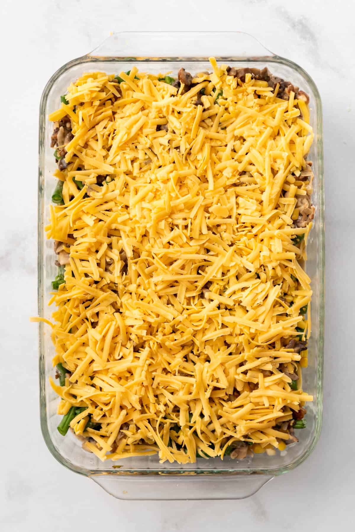 Shredded cheese sprinkled over ground beef and vegetable filling in a casserole dish.