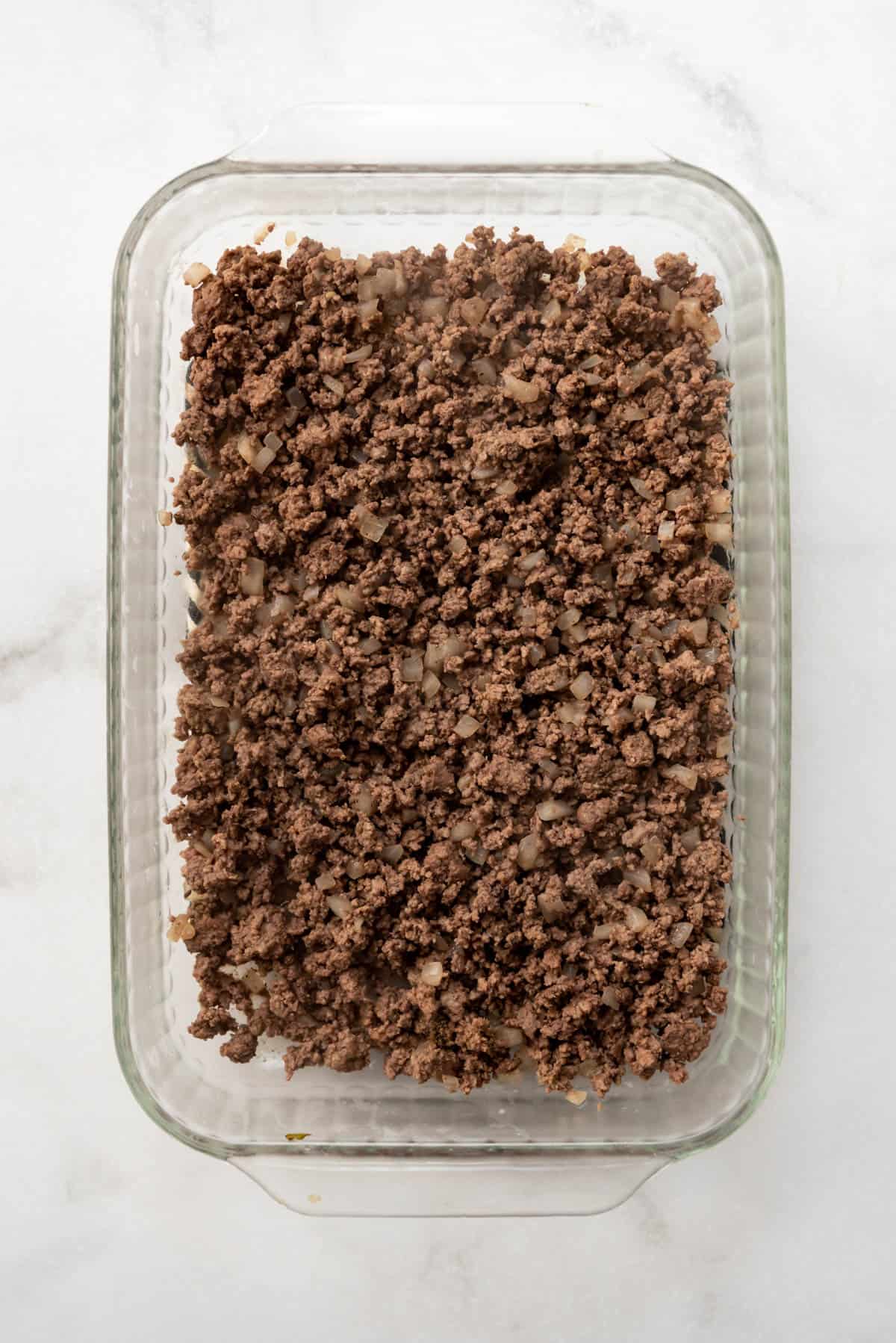 A layer of ground beef in a casserole dish.