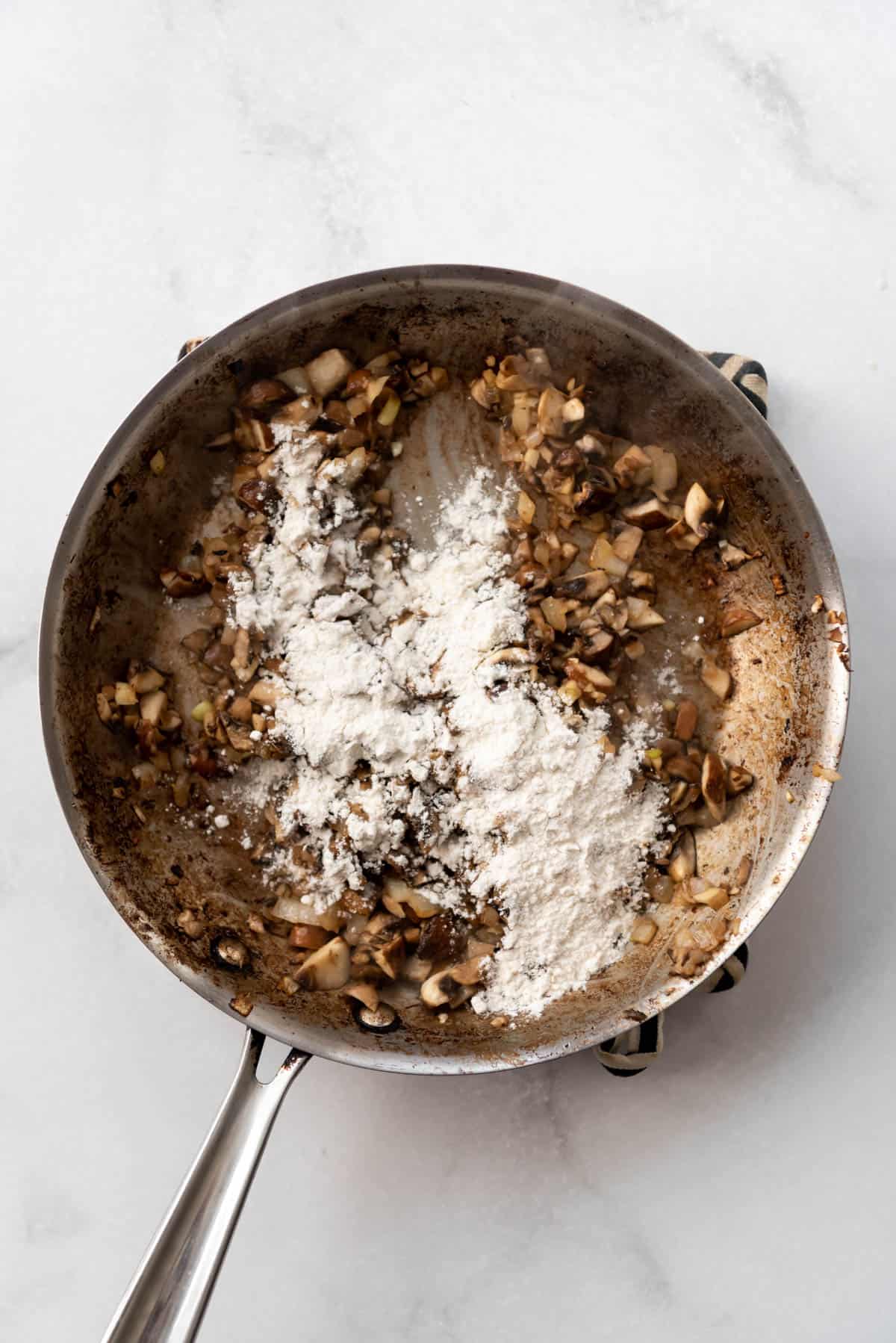 Flour sprinkled over sauteed mushrooms in a pan.