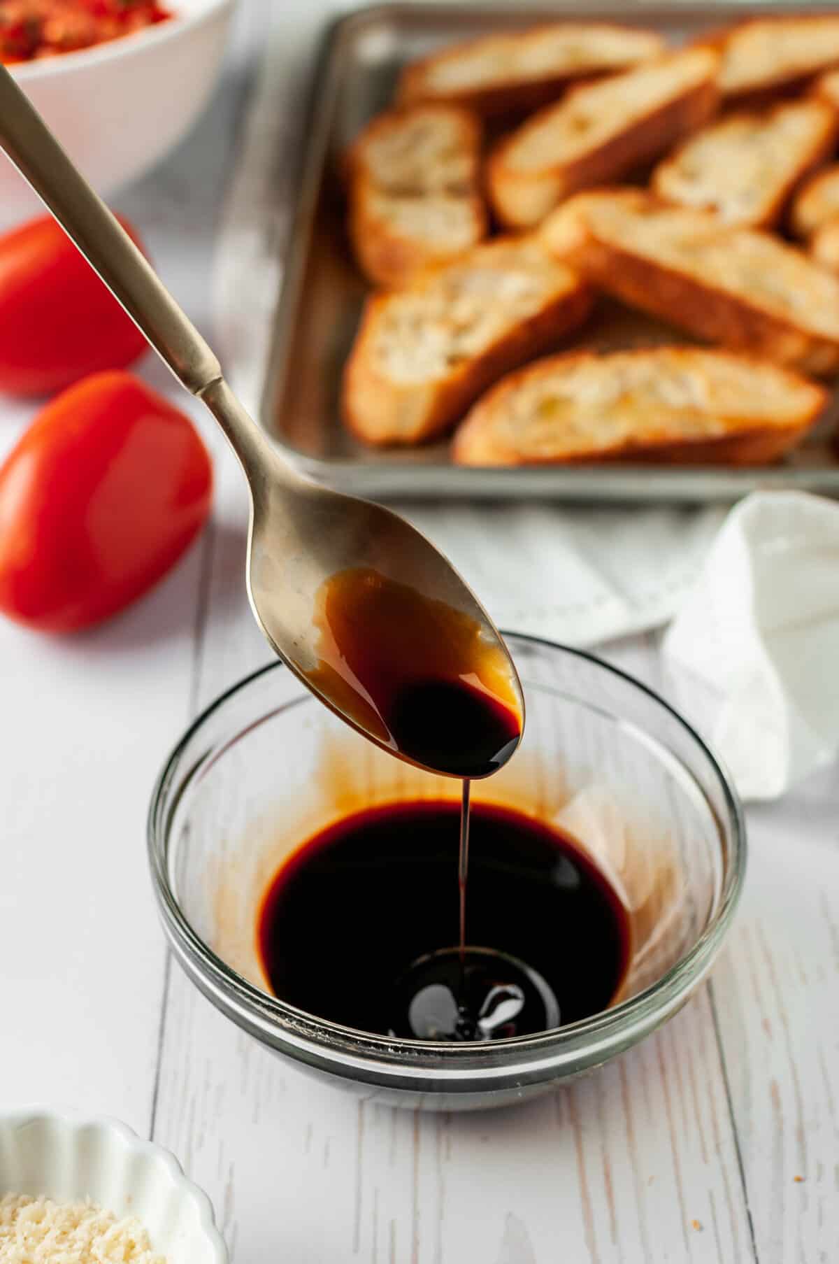 Spoon of balsamic reduction dripping into small glass bowl