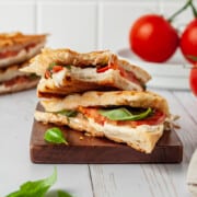Two caprese panini halves stacked on wood board