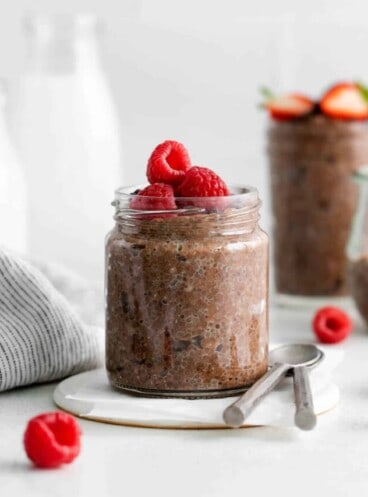 Chocolate chia seed pudding in a glass jar with raspberries on top.