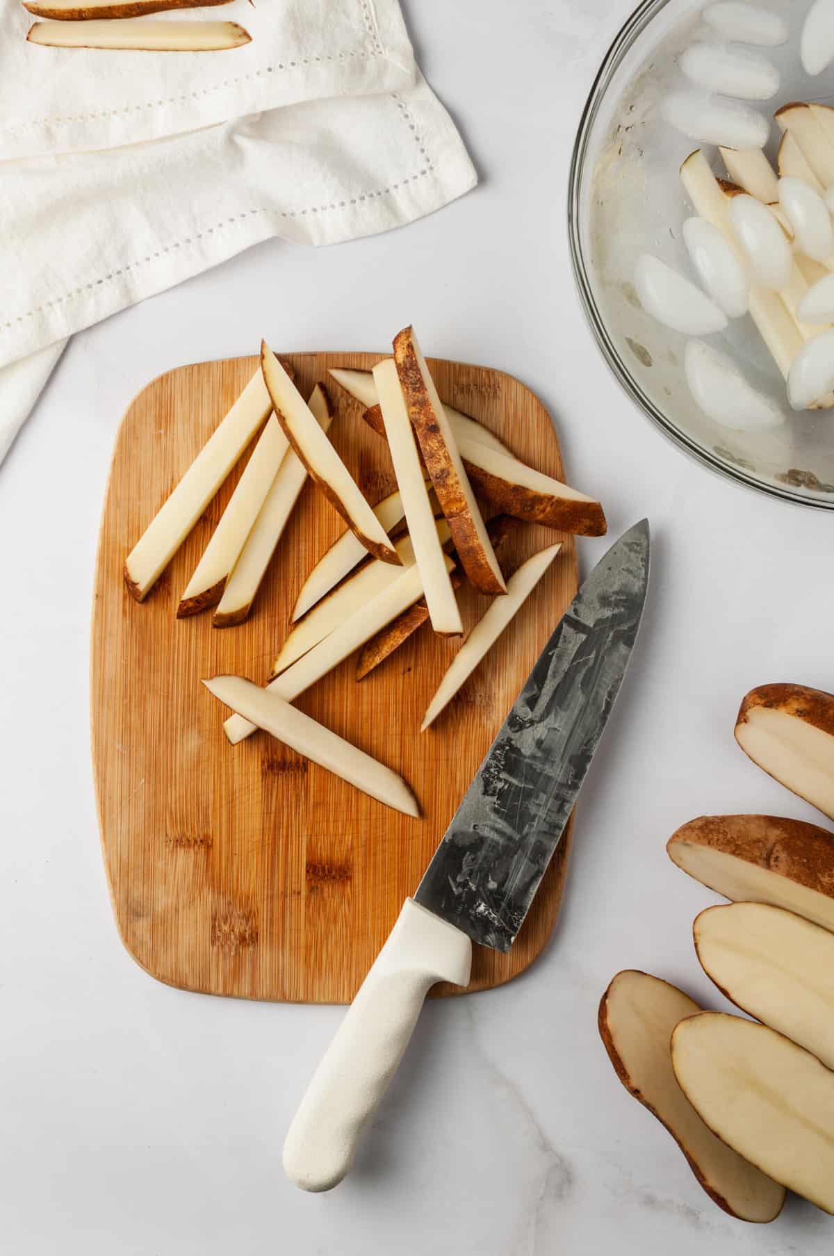 Overhead view of potatoes cut into fries on wood board